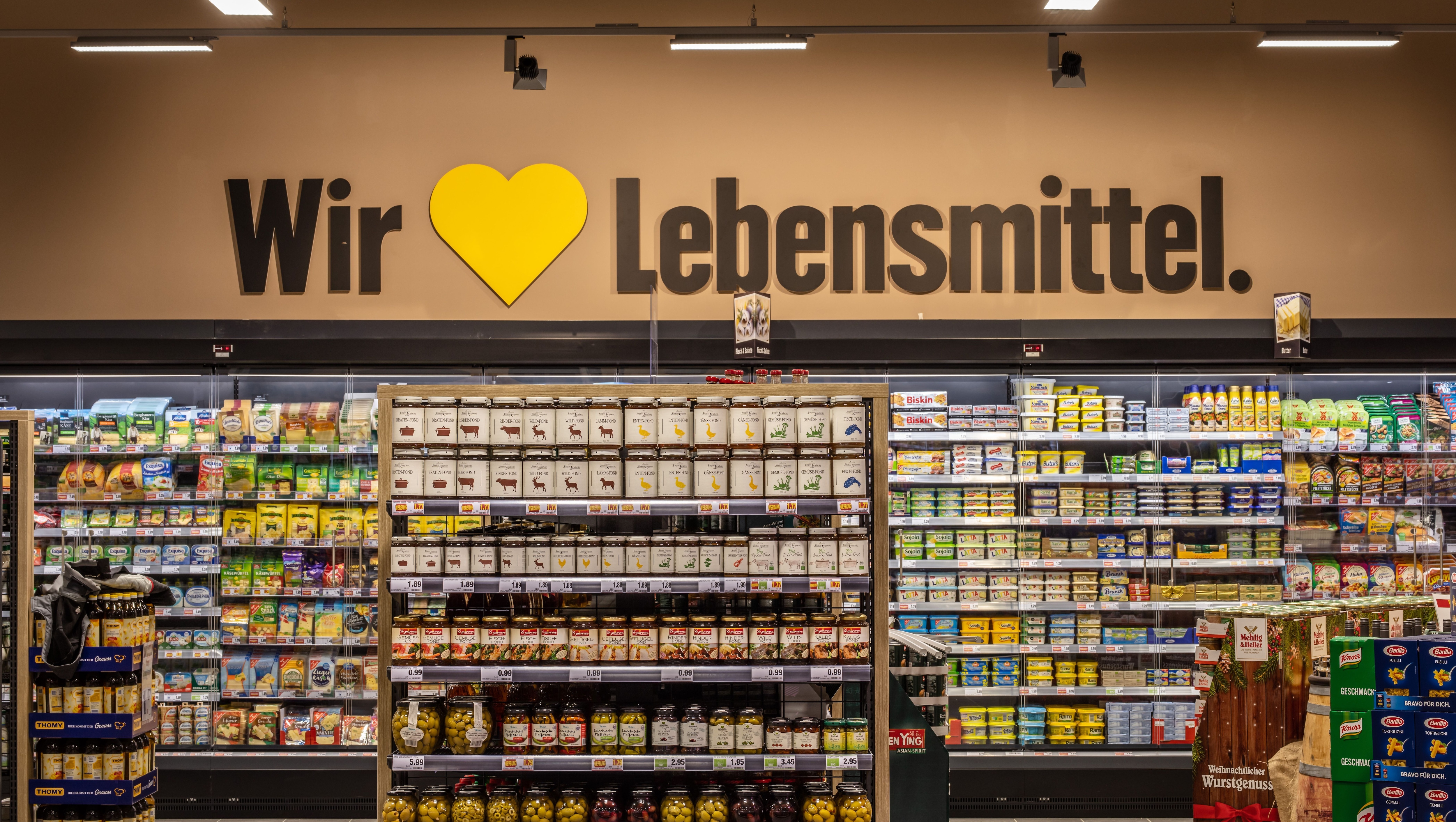 Kühlregal mit Molkereiprodukten und an der Wand obedrüber ist ein großer Schriftzug mit "Wir lieben Lebensmittel".