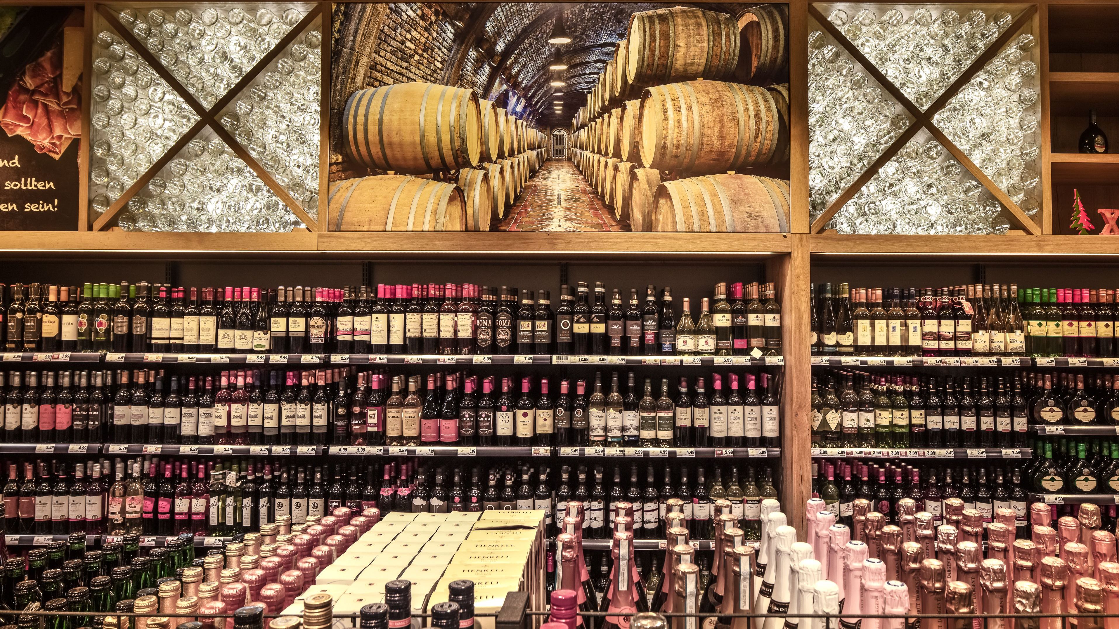 Im Vordergrund sieht man angeschnitten die Sektflaschen und im Hintergrund das Regal mit Rotweinen.