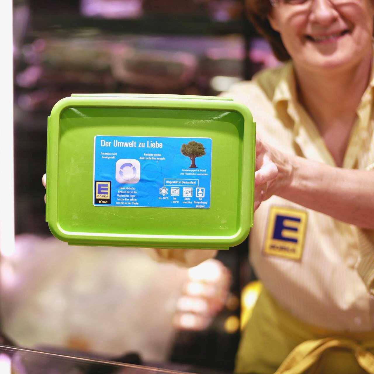 Eine Mitarbeiterin hält eine Plastikbox auf der "Der Umwelt zur Liebe" steht.