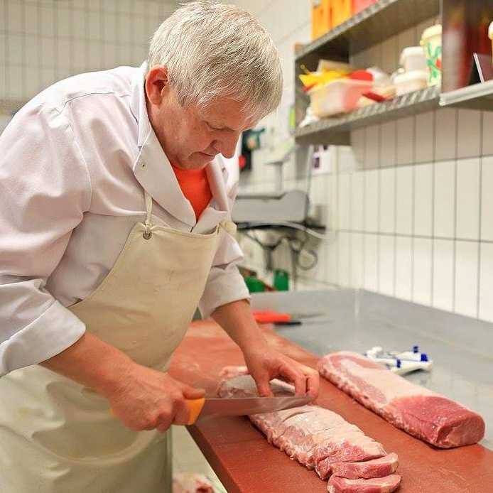 Ein Fleischereimitarbeiter schneidet ein Stück Fleisch mit einem Messer.