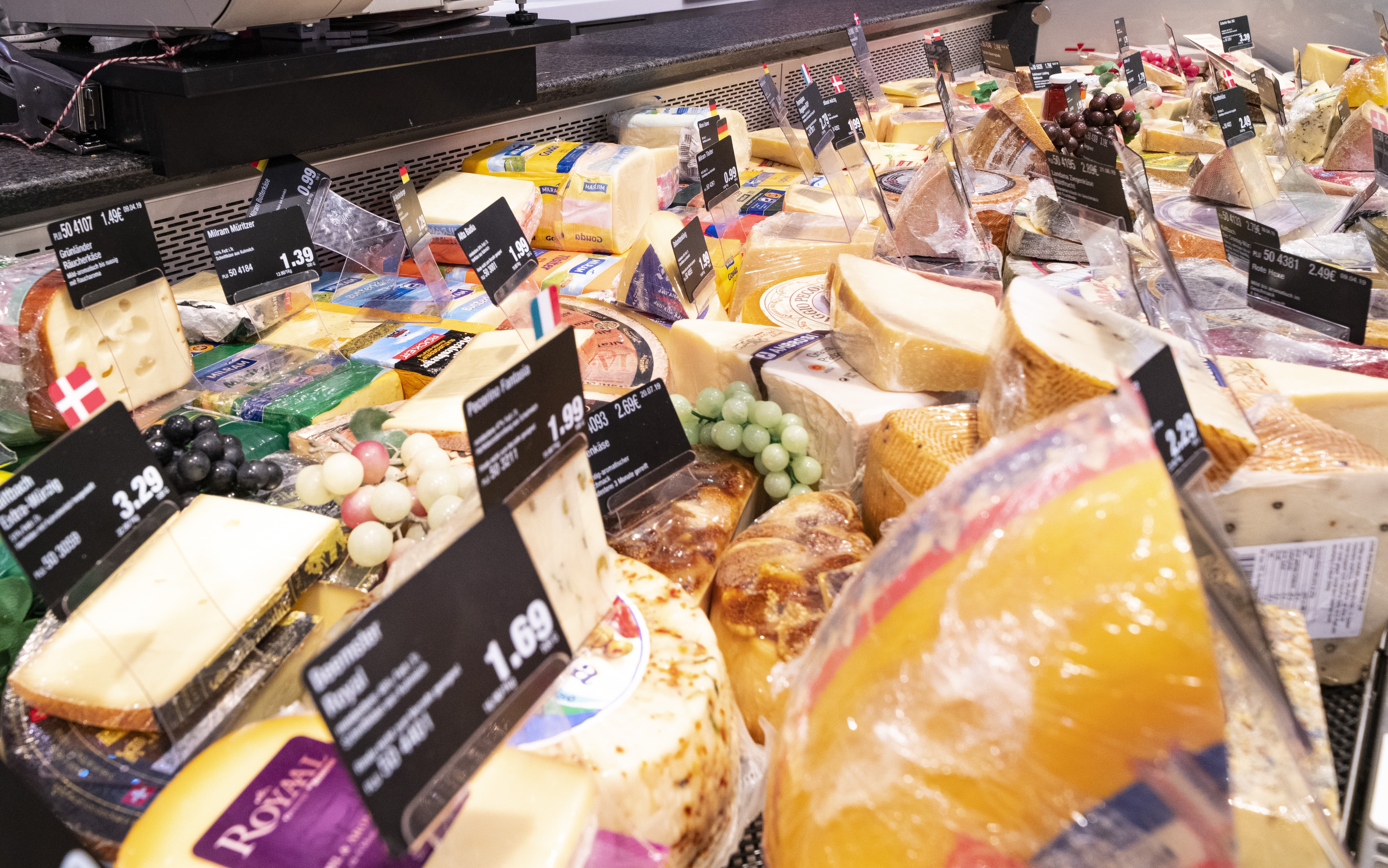 Käseauslage einer Bedienungstheke mit vielen verschiedenen Käsesorten und Preisschildern.