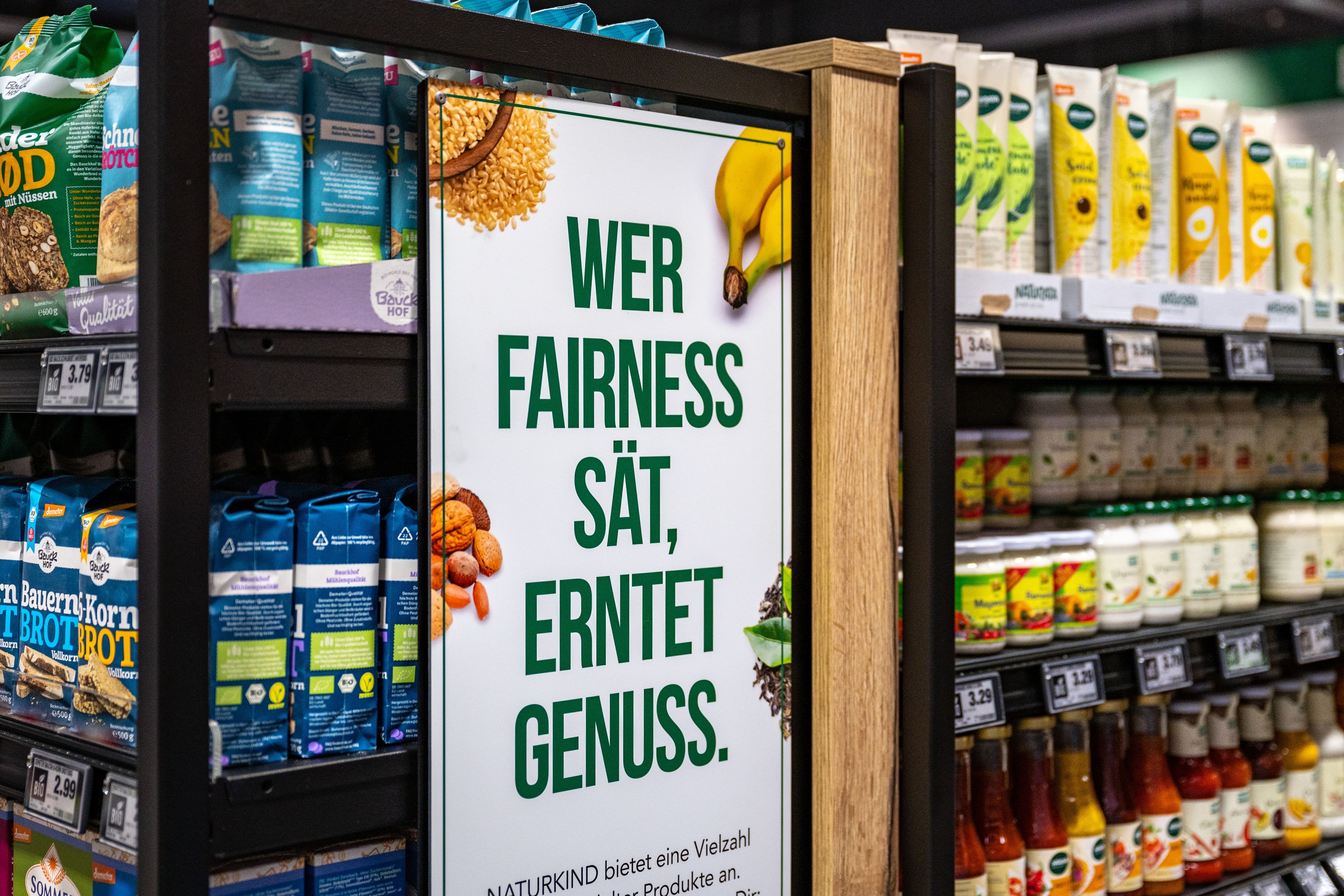 Ein Schild an einem Regal in einem Supermarkt. Auf dem Schild steht: "Wer Fairness sät, erntet Genuss".