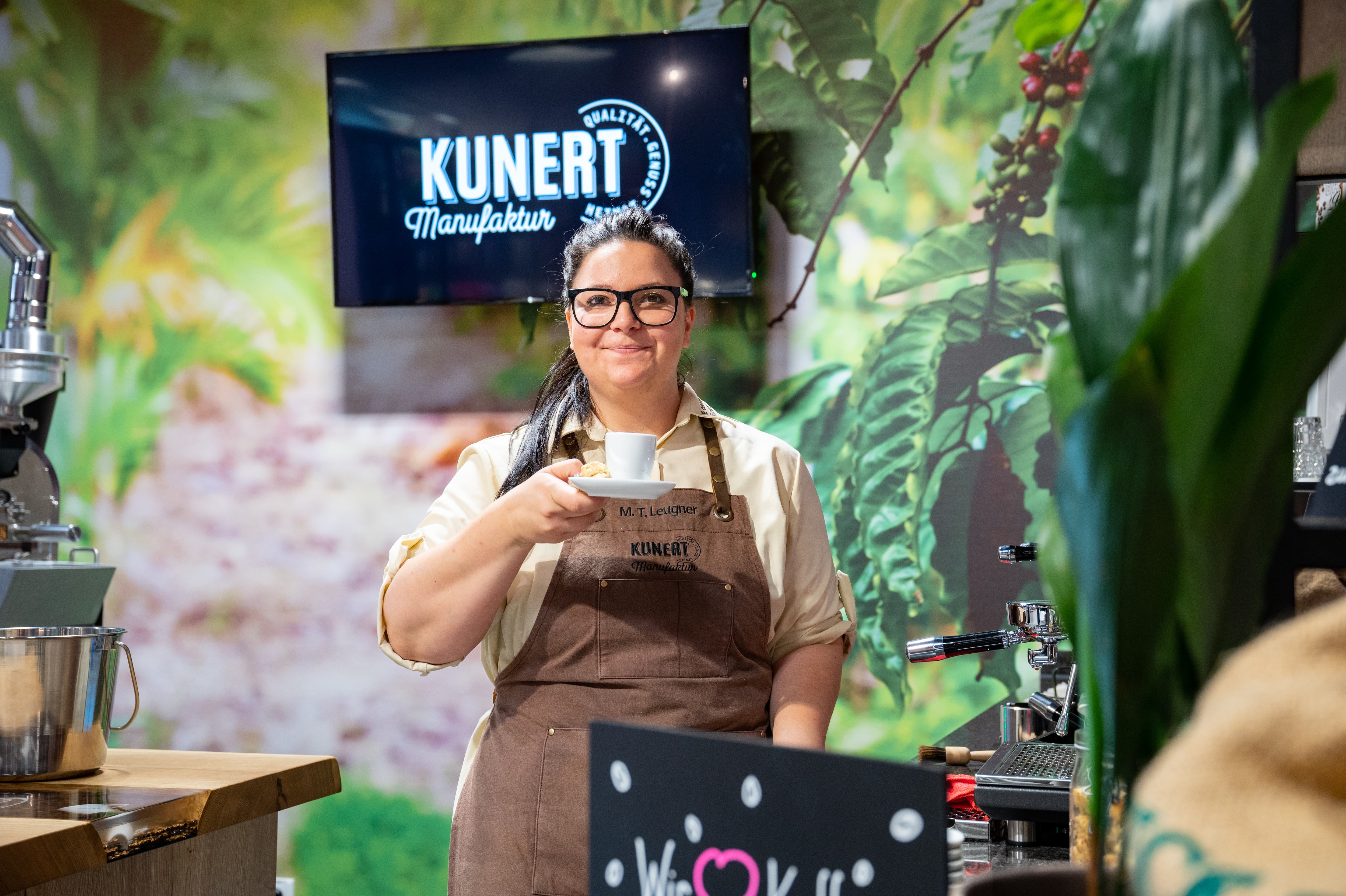 Eine Mitarbeiterin einer Kaffeerösterei hält eine Tasse in der Hand und lächelt.