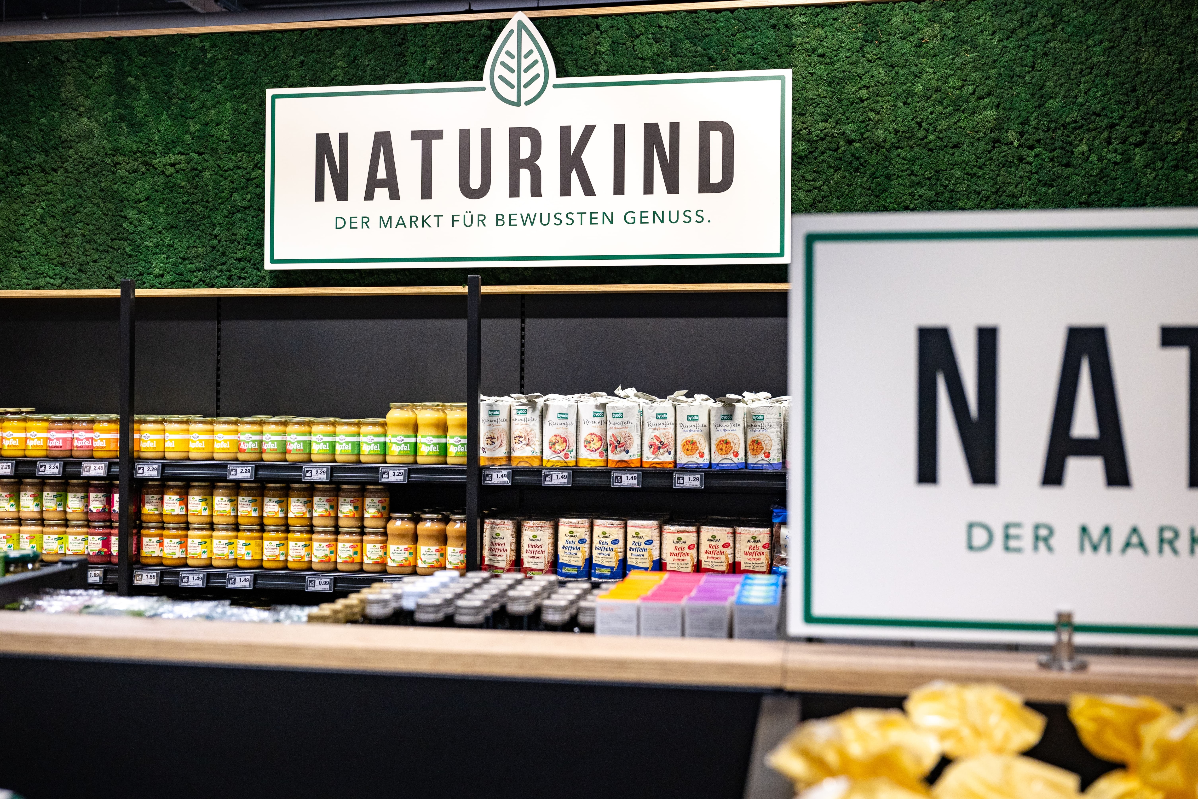 Ein Regal mit Bio-Produkten über dem ein Schild angebracht ist. Auf dem Schild steht: "Naturkind - Der Markt für bewussten Genuss"