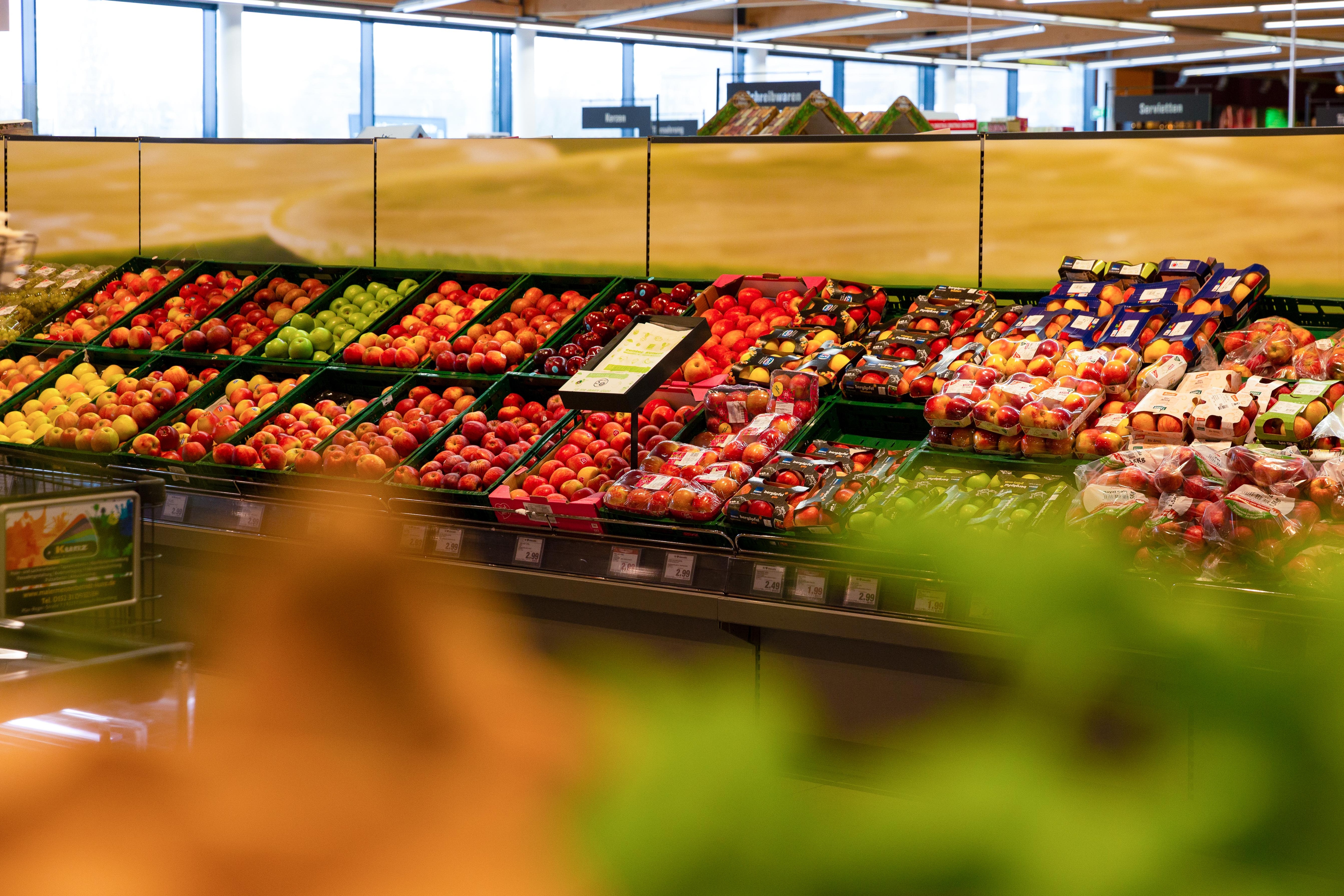 Ein Regal mit Kisten voller verschiedener Apfelsorten in der Obstabteilung eines Edeka-Marktes.