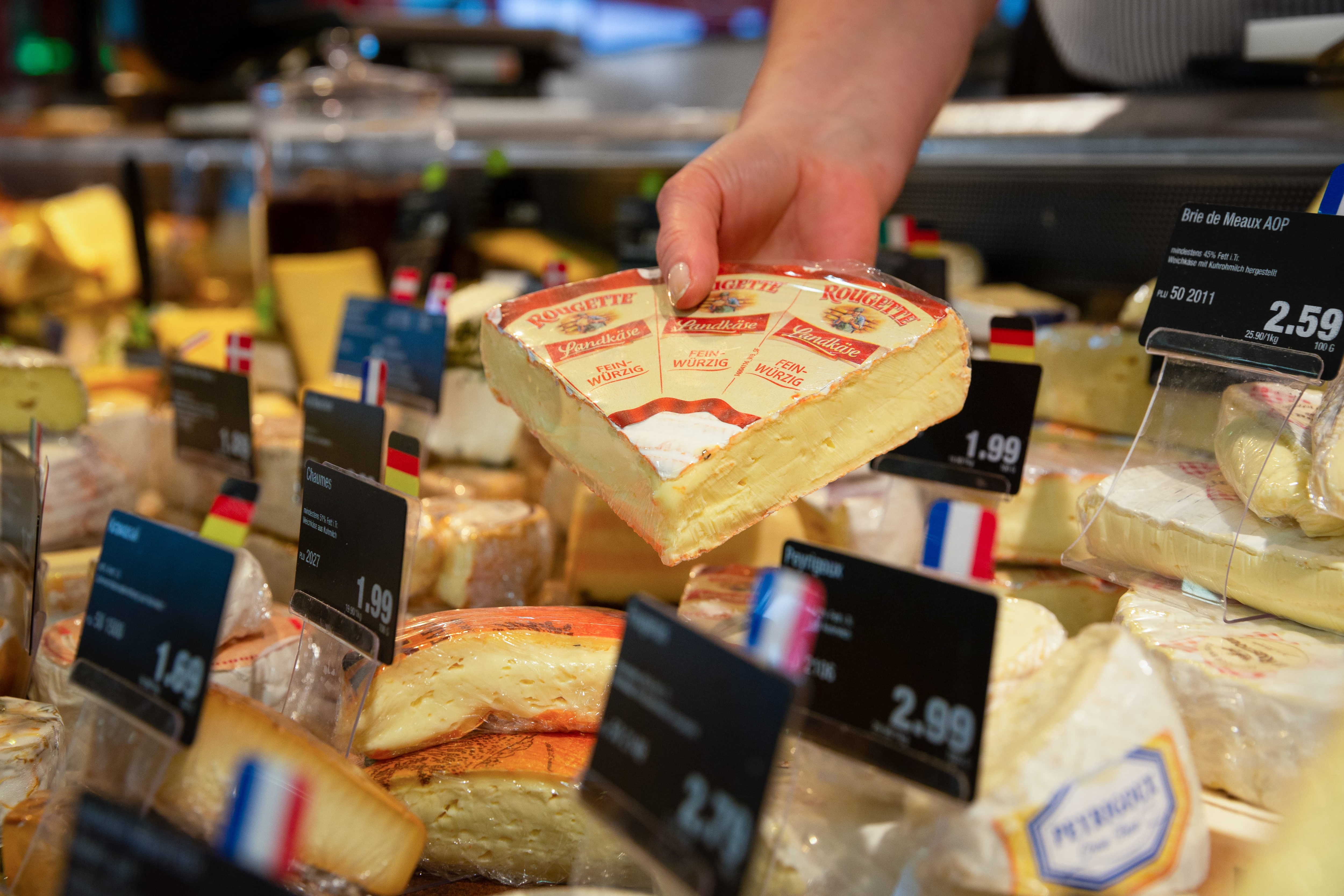 Eine Hand nimmt ein Stück Käse aus der Auslage einer Frischetheke.