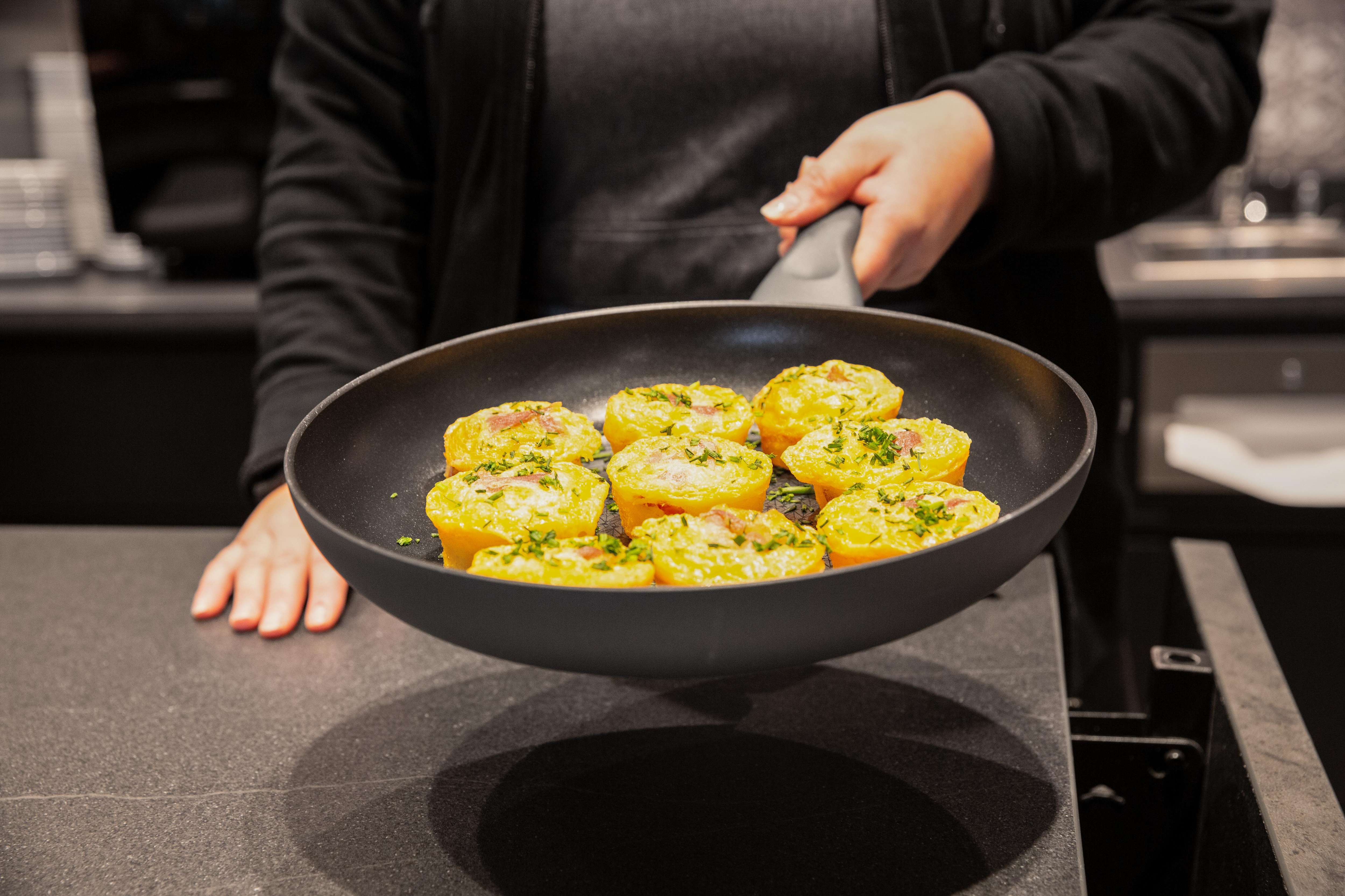Eine Frau hält eine Pfanne mit frisch zubereiteten Essen in der Hand.