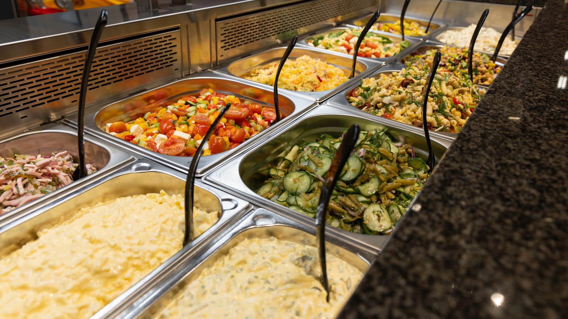 Salatbar mit verschiedenen Salatvarianten wie z.B. Kartoffel-, Nudel-, Gurken-, Tomaten- und Nudelsalat mit unterschiedlichen Zutaten