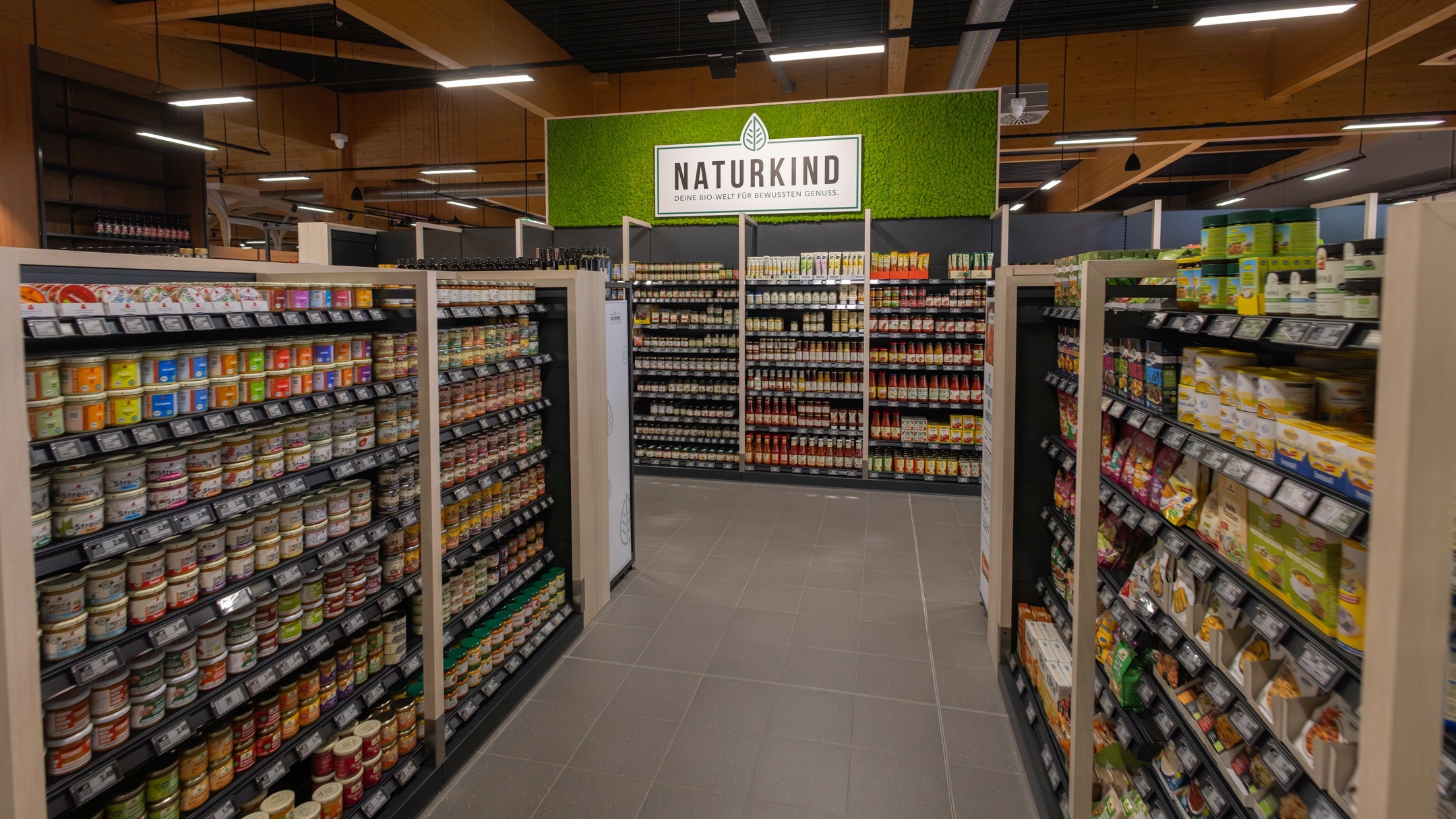 Zugang zum Bereich "Naturkind" mit 2 Produktregalen auf der linken und rechten Seite und dem Naturkind-Produkt-Regal am Ende des Ganges