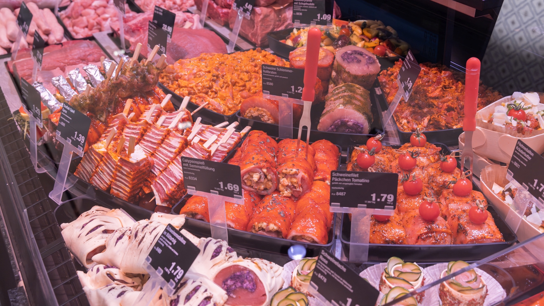 Fleisch-Bedientheke mit verschiedenen Fleischangeboten wie Schweinefilet Päckchen Tomatino, Calypsospieß mit Semmelfüllung, Schweine Schlemmer Rollbraten, Gyros und Filetmedaillons mit Kräuterbutter. Im Hintergrund weitere Angebote wie Filetspitzen, Gulasch und Kotelett