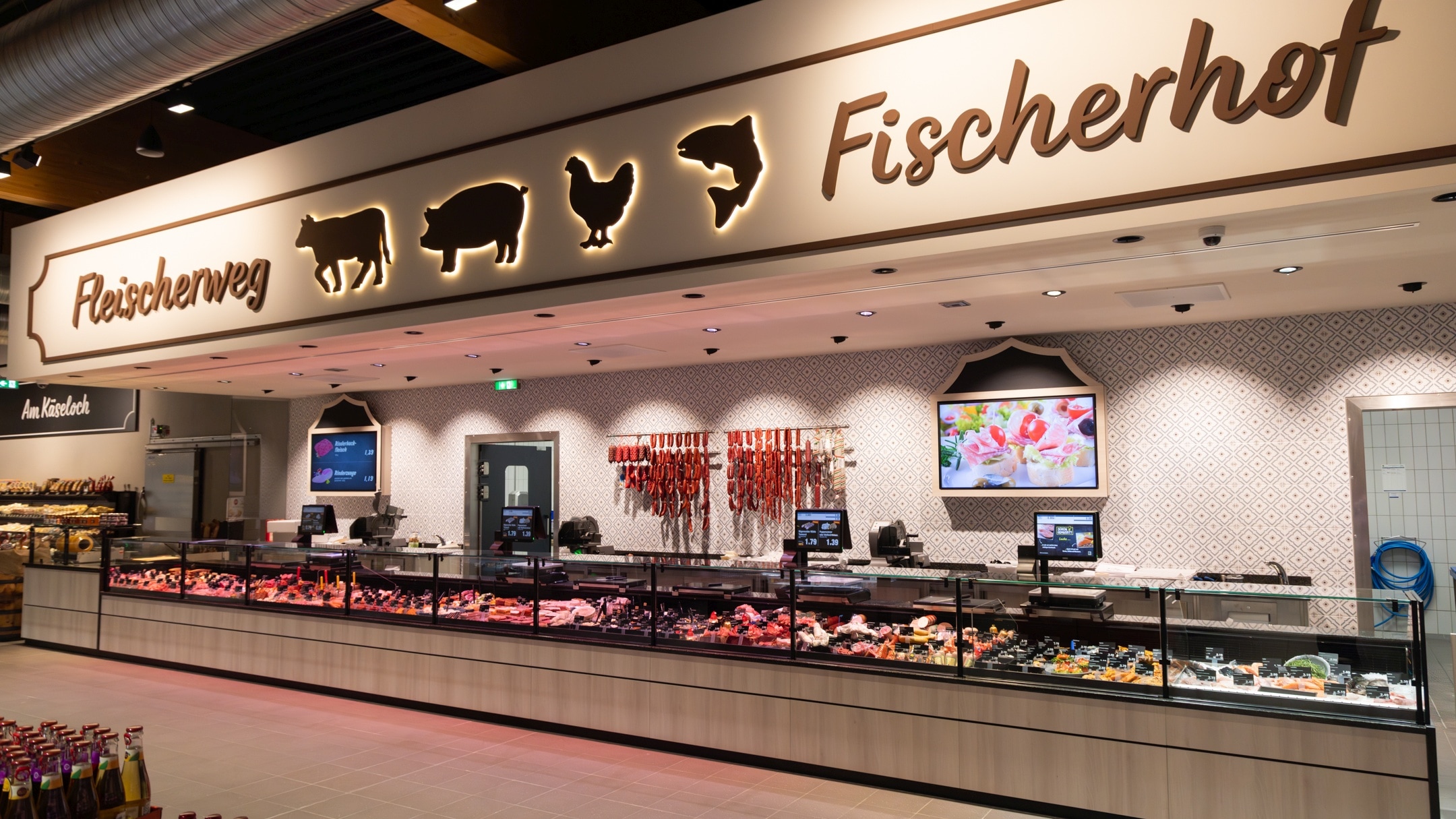 Frontansicht der Frischtheke "Fleischerweg und Fischerhof". An der Wand hängen verschiedene Wurststränge und 2 Werbetafeln, in der Frischetheke selbst werden die Fleisch-, Wurst-, Salat- und Fischsorten angeboten