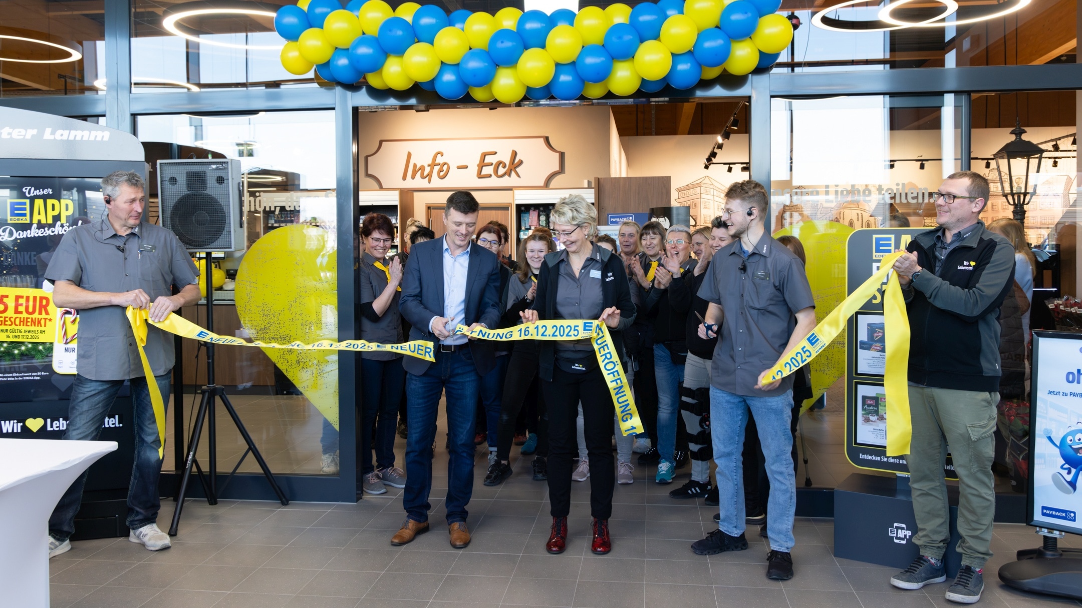 Edeka-Mitarbeiter zerschneiden bei der Neueröffnung des Marktes am 16. Dezember 2025 das Gelbe Band vor der Eingangstür. Im Hintergrund weiter applaudierende Mitarbeiter und Kunden