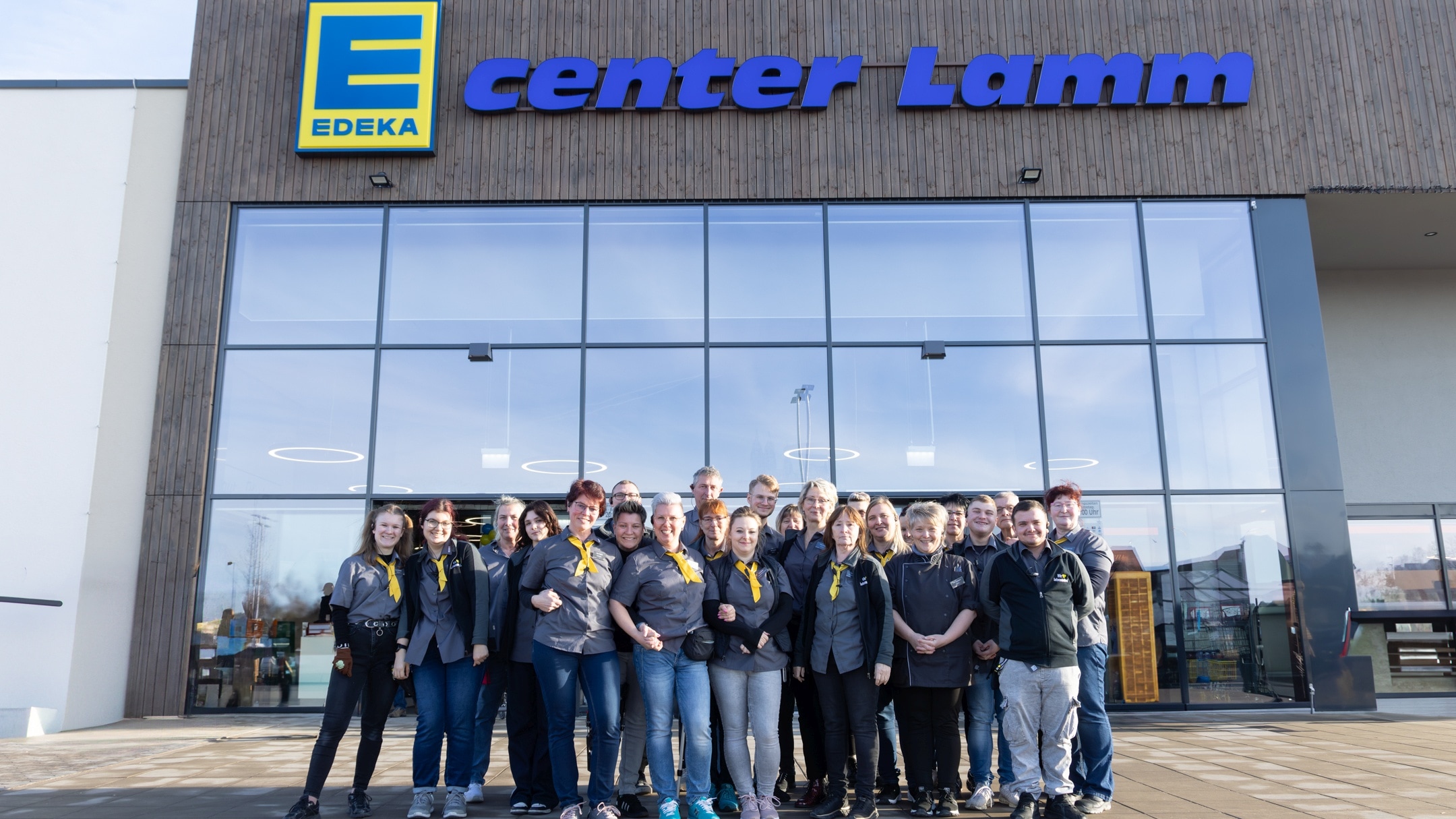 Gruppenfoto der Ecenter Lamm Eigentümer und Mitarbeiter vor der Glasfront am Eingangsbereich des Marktes