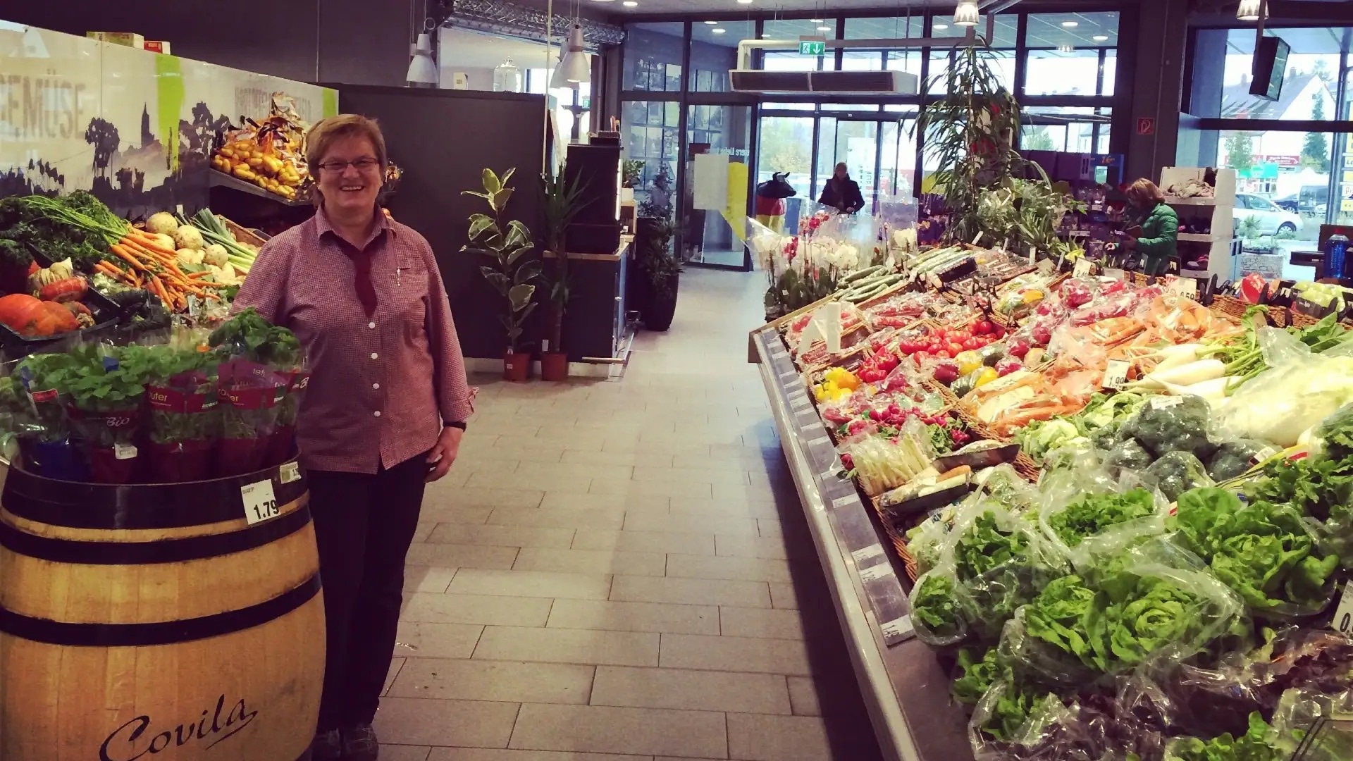 Eine lächelnde Mitarbeiterin steht in der Obst- und Gemüseabteilung eines EDEKA-Marktes.