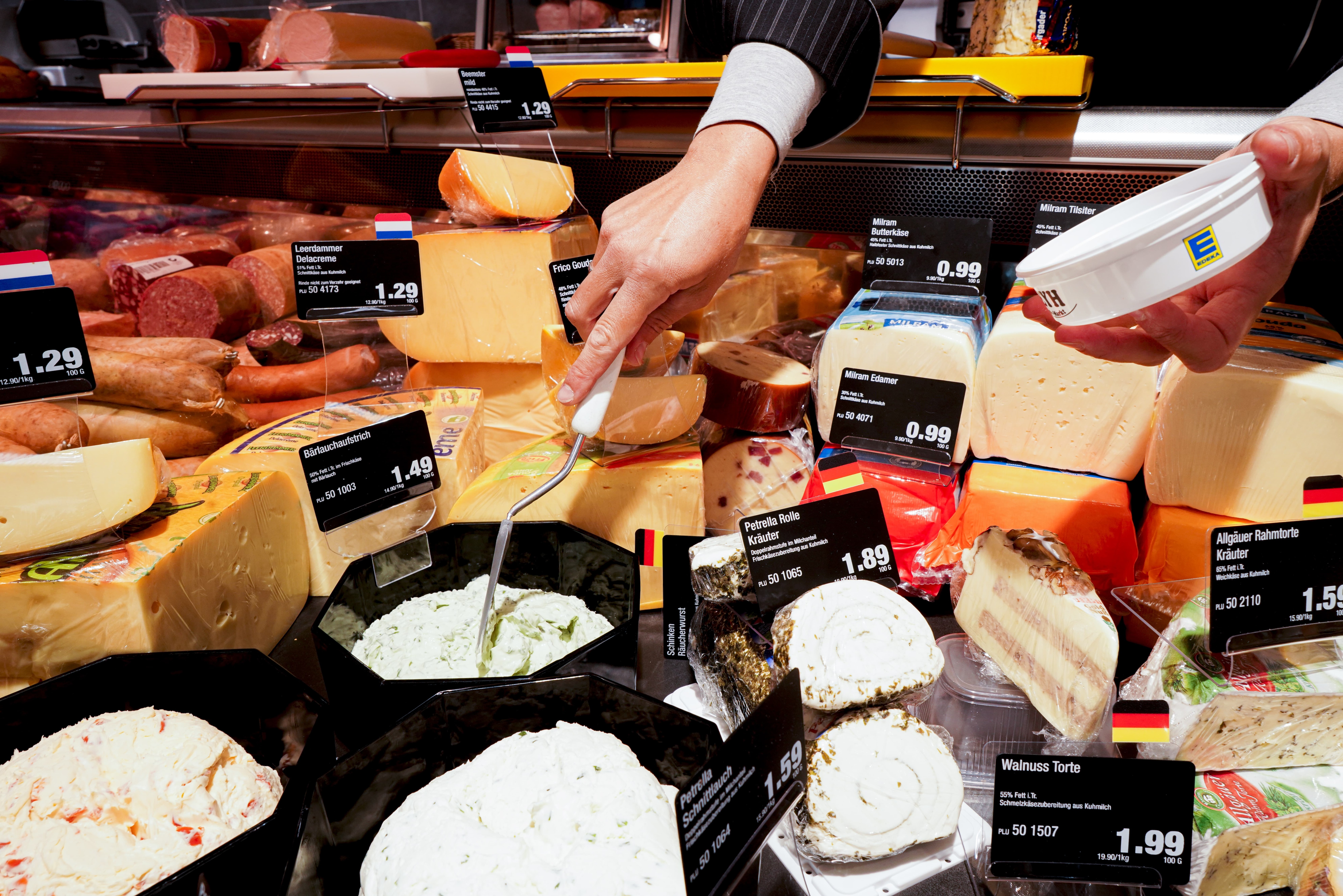 Käseauslage einer Bedienungstheke mit vielen verschiedenen Käsesorten und Preisschildern.