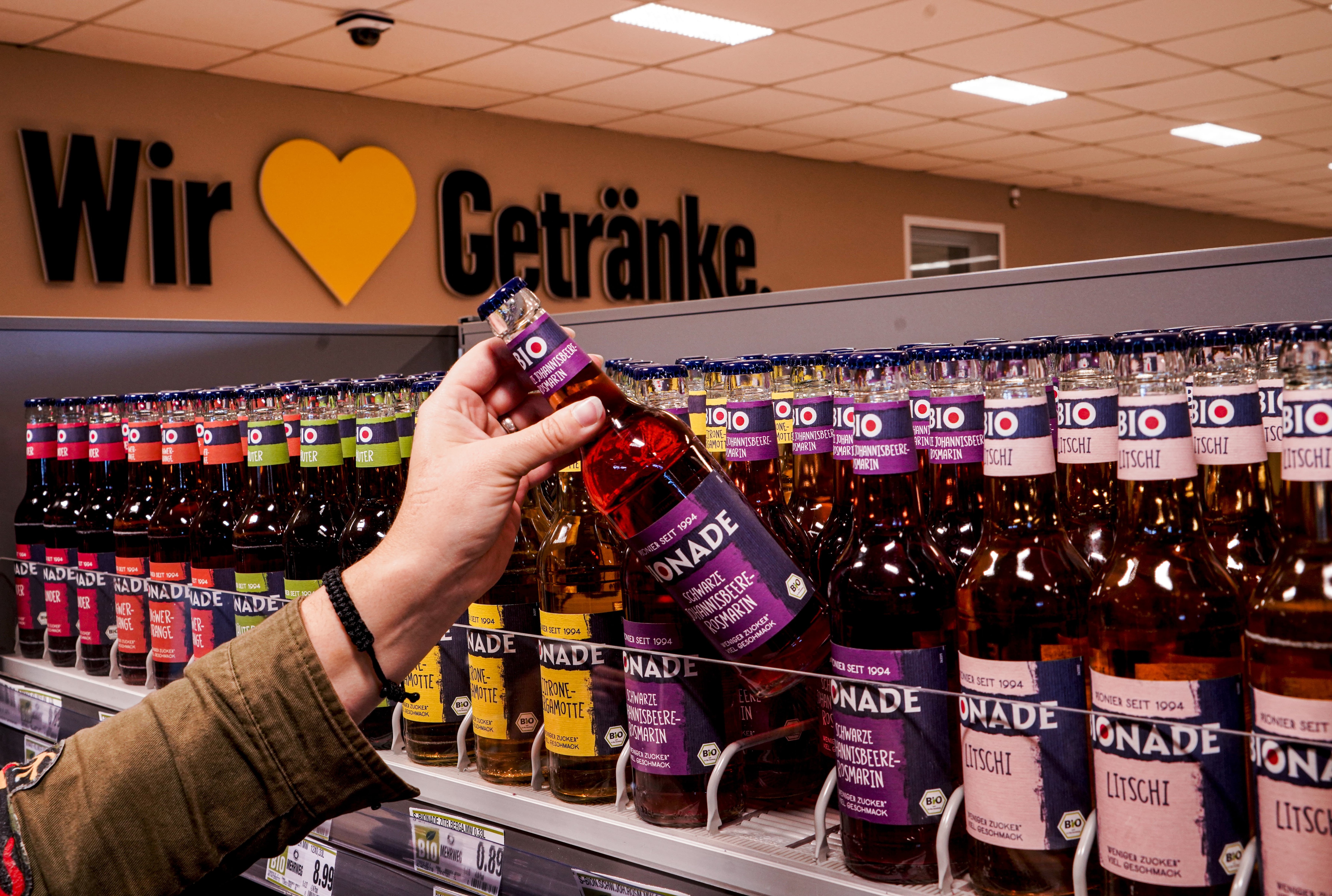 Eine Hand nimmt eine Flasche Bionade aus einem Regal voller Bionade-Flaschen.