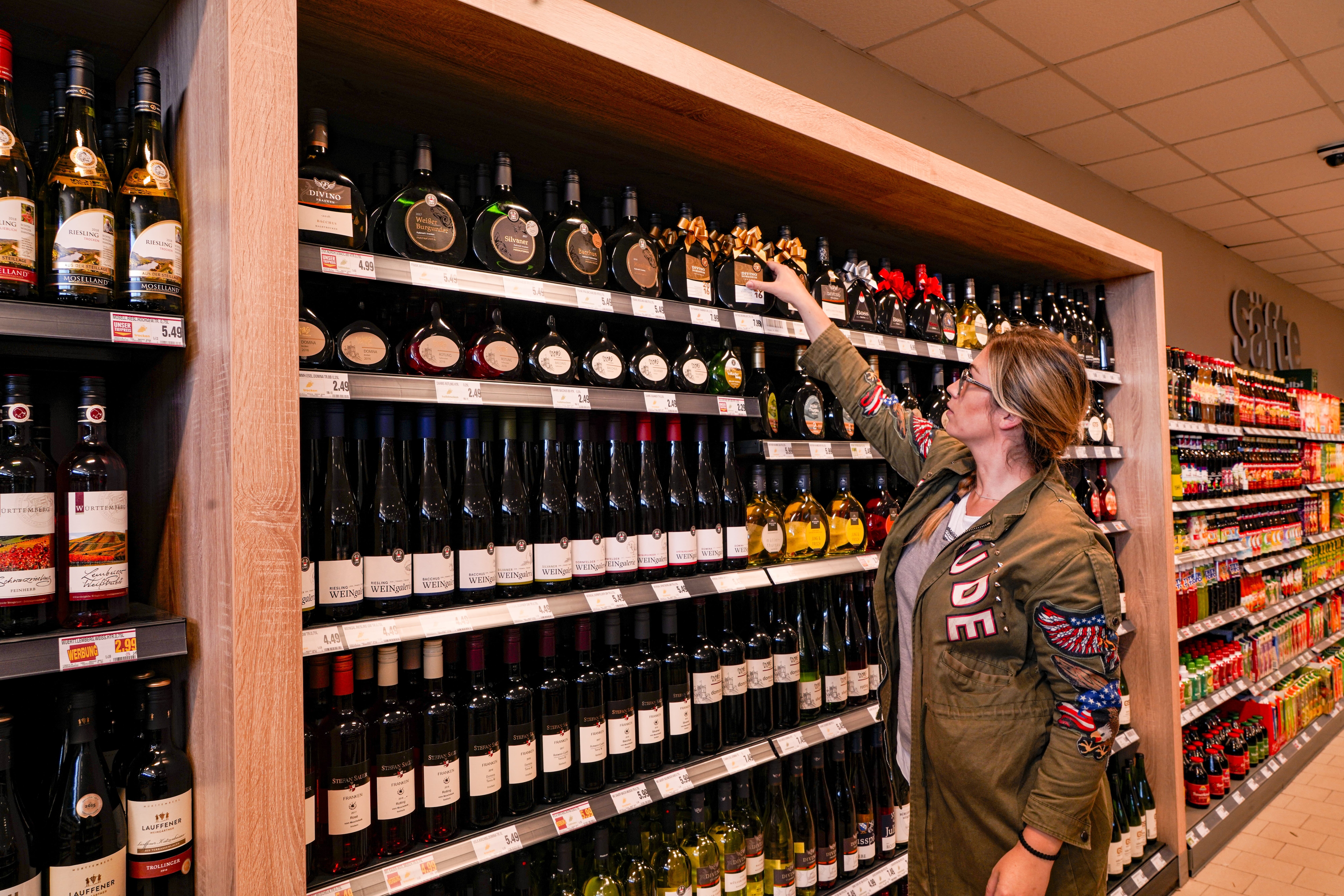 Eine Kundin steht in der Weinabteilung eines EDEKA-Markts und greift nach einer Flasche.