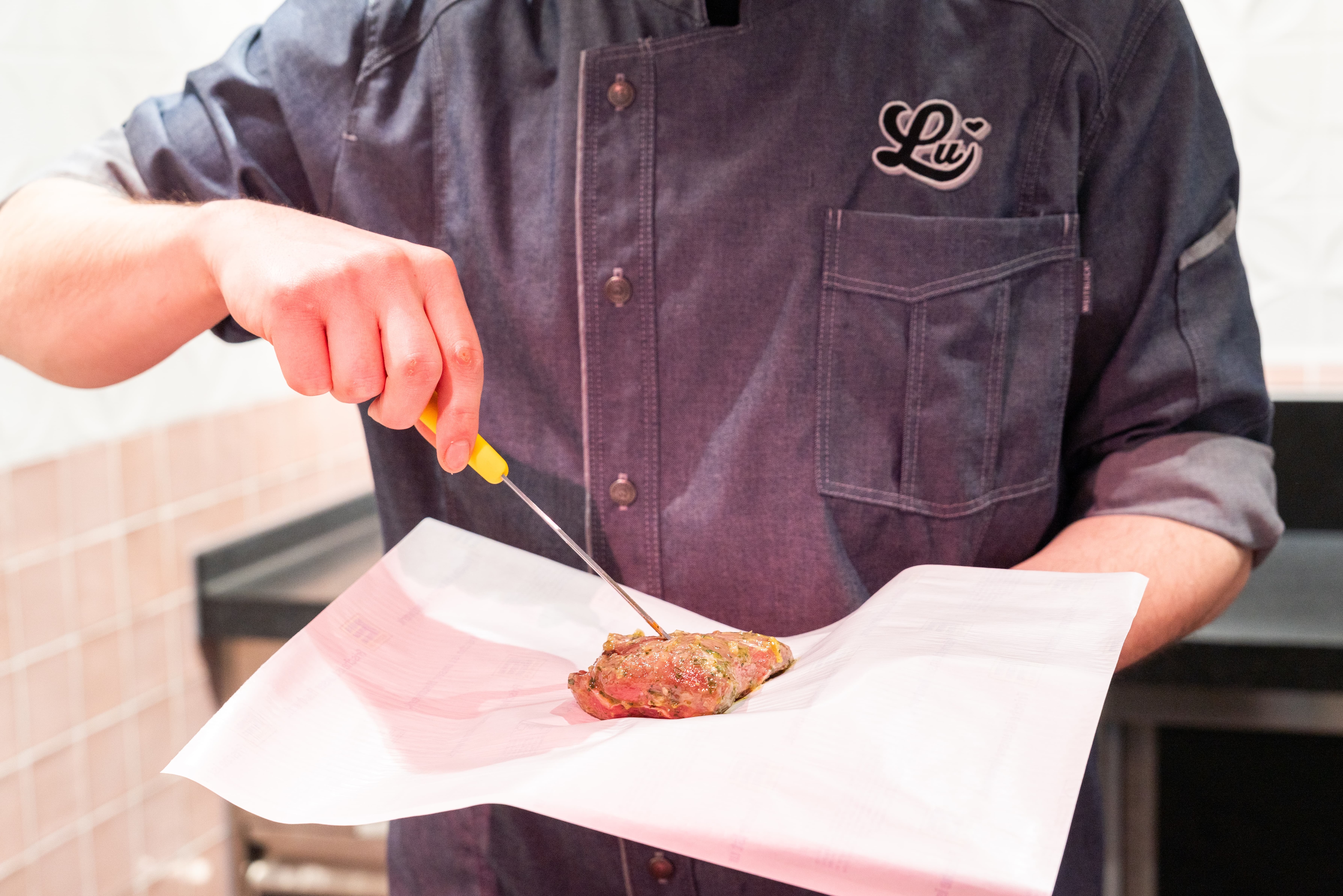 Ein Mitarbeiter legt ein Stück mariniertes Fleisch auf ein Stück Papier.