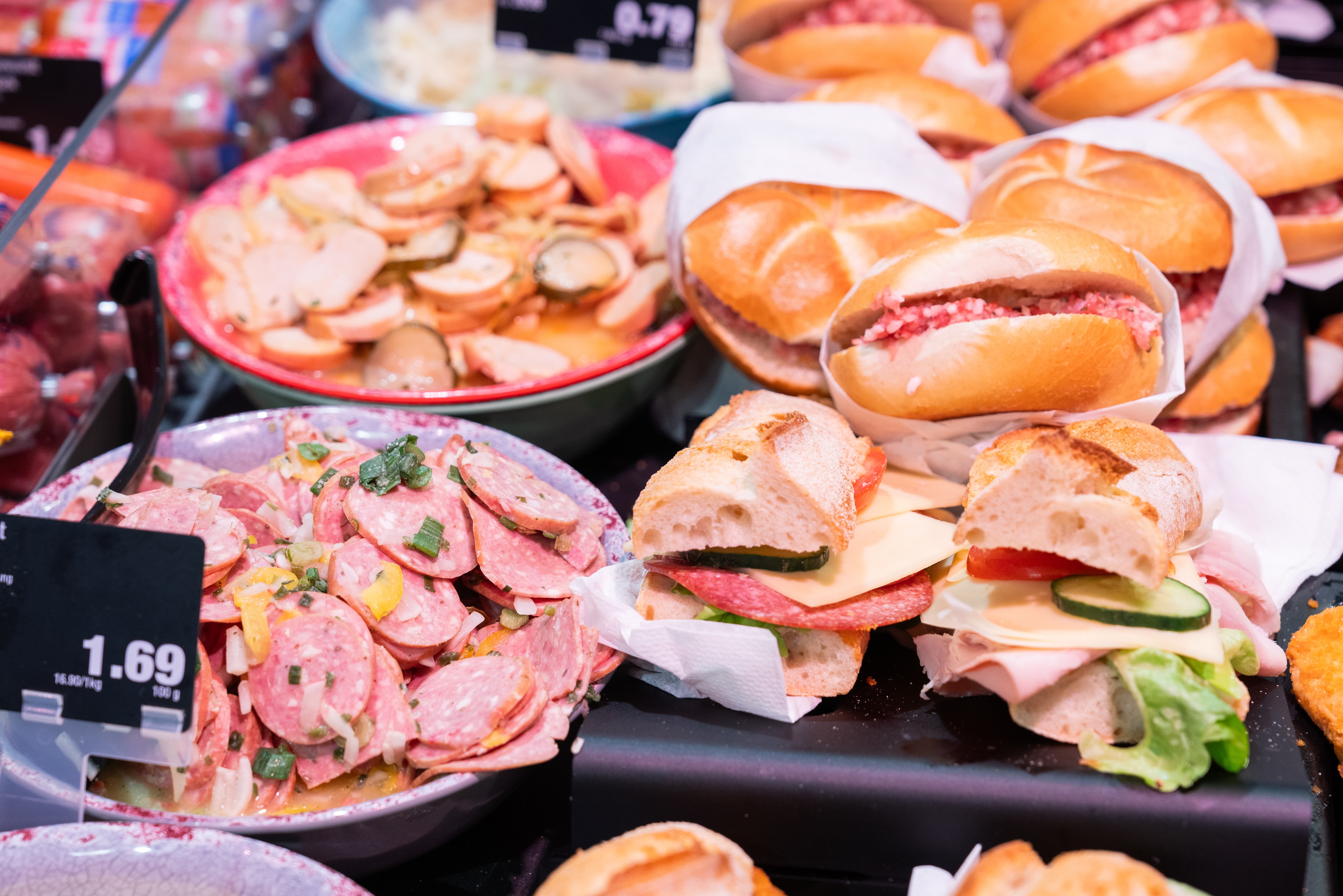 Eine Schale Wurstsalat sowie verschieden belegte Brötchen in einer Auslage.