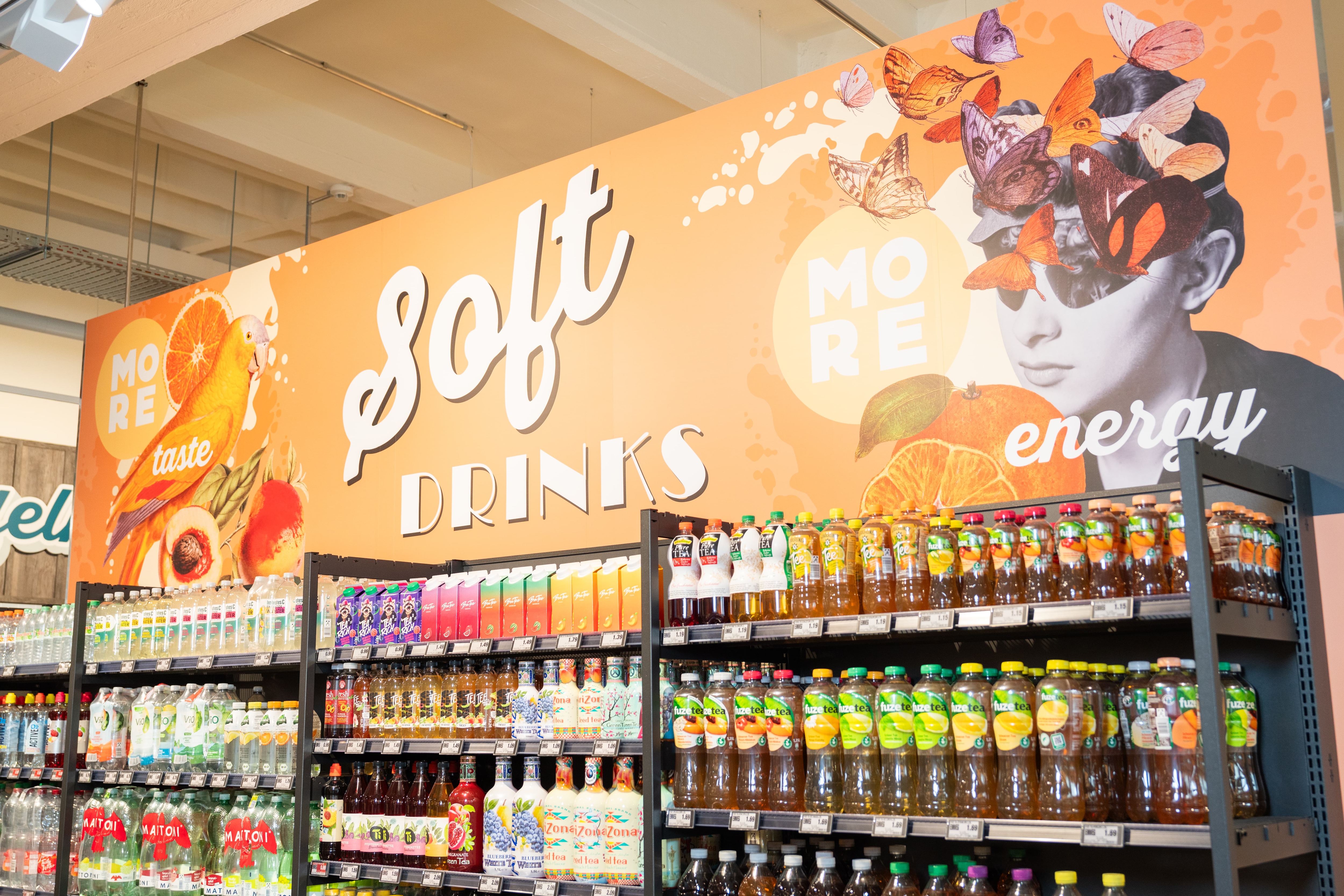 Regale mit Softdrinks. Darüber eine farbenfrohe Grafik mit der Aufschrift: "Softdrinks".