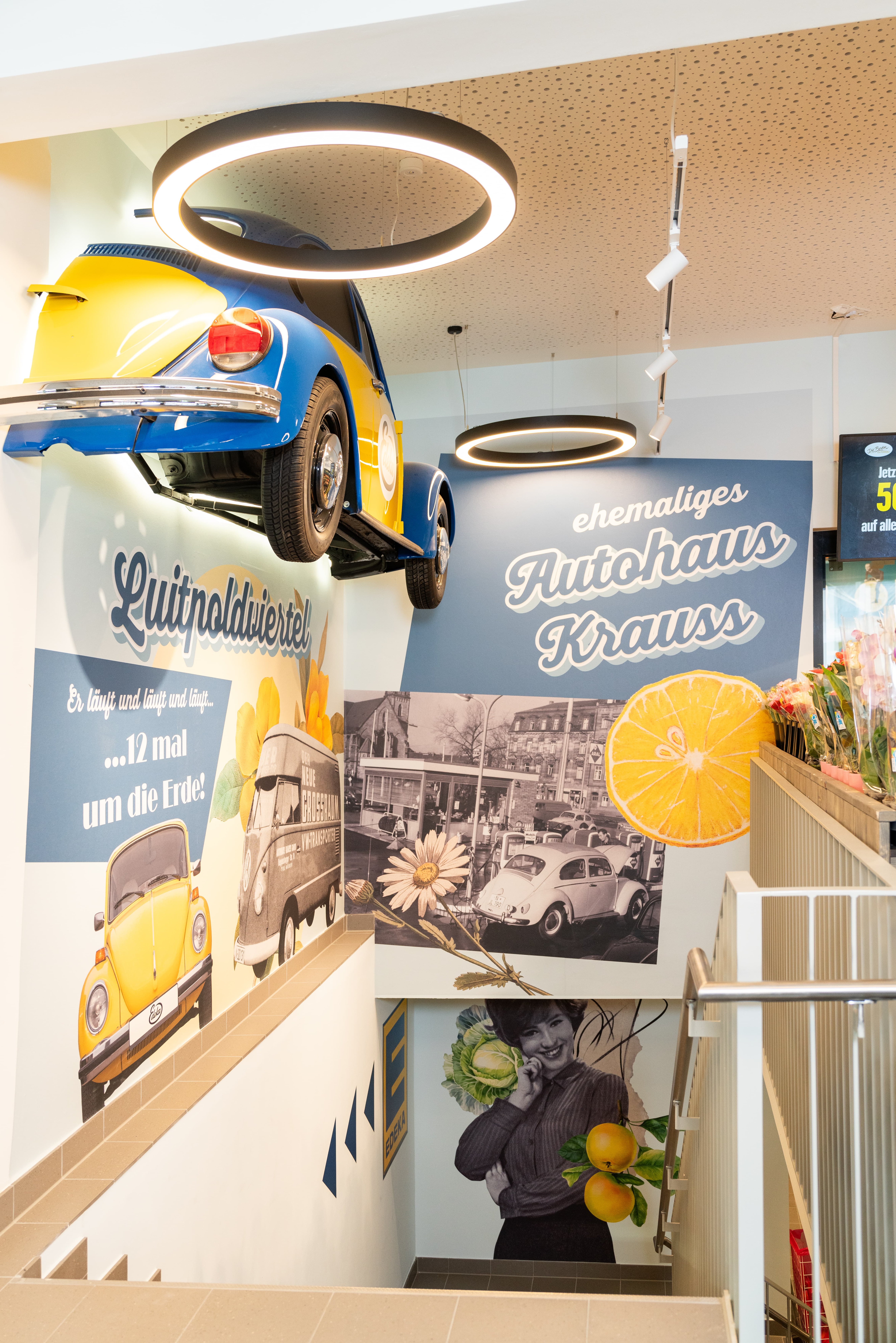 Ein Treppenaufgang über dem an der Wand ein halber blau-gelber VW-Käfer angebracht ist.