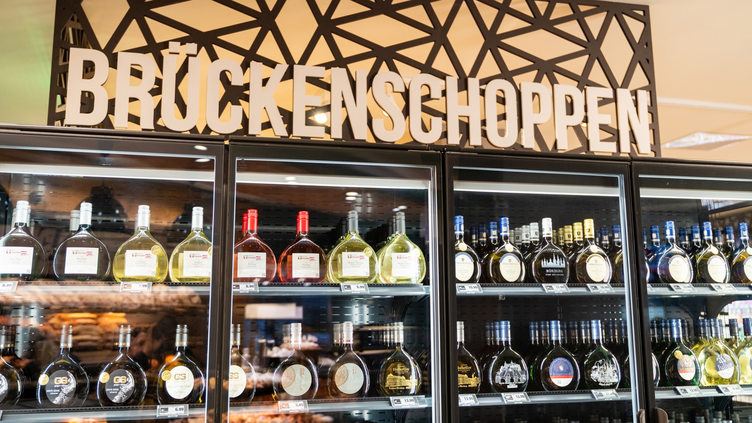 Teilansicht eines Weinregals mit "Kühlfunktion" . Hier werden verschiedene Wein-Anbieter und Sorten unter dem Namen "Brückenschoppen" angeboten