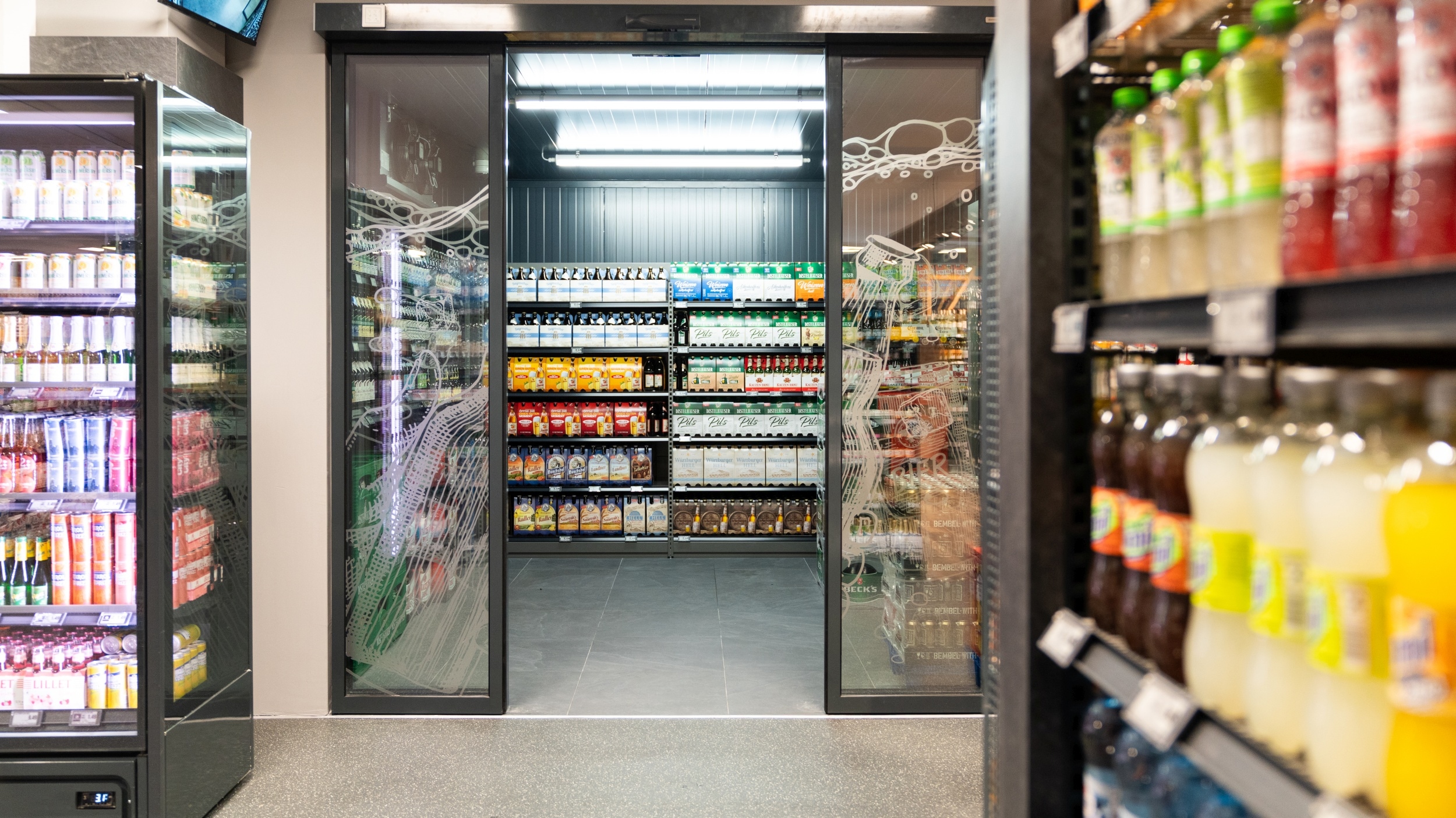 Durchgang zur separaten Alkohol- und Spirituosen-Abteilung mit Blick auf ein Regal mit Sechserpack unterschiedlicher Biersorten