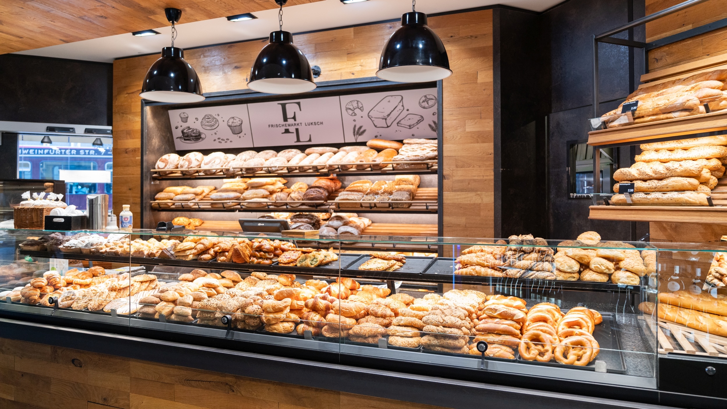 Front-Ansicht der Bäckereiabteilung mit der Bedientheke. Angeboten werden verschiedene Brote, Brötchen, Brezeln und Croissants