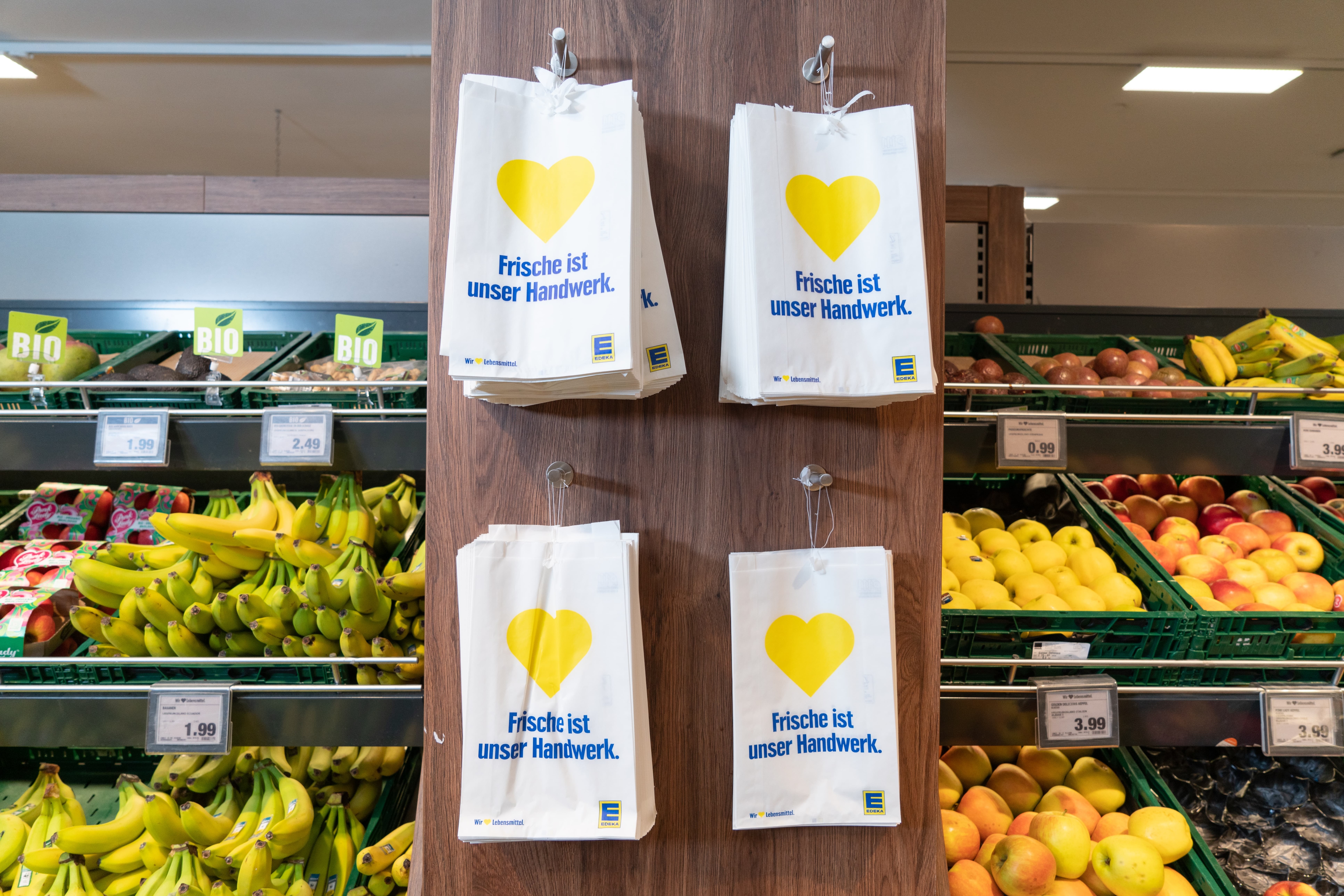 Vier Haken an denen Stapel von Papiertüten für Obst und Gemüse hängen.