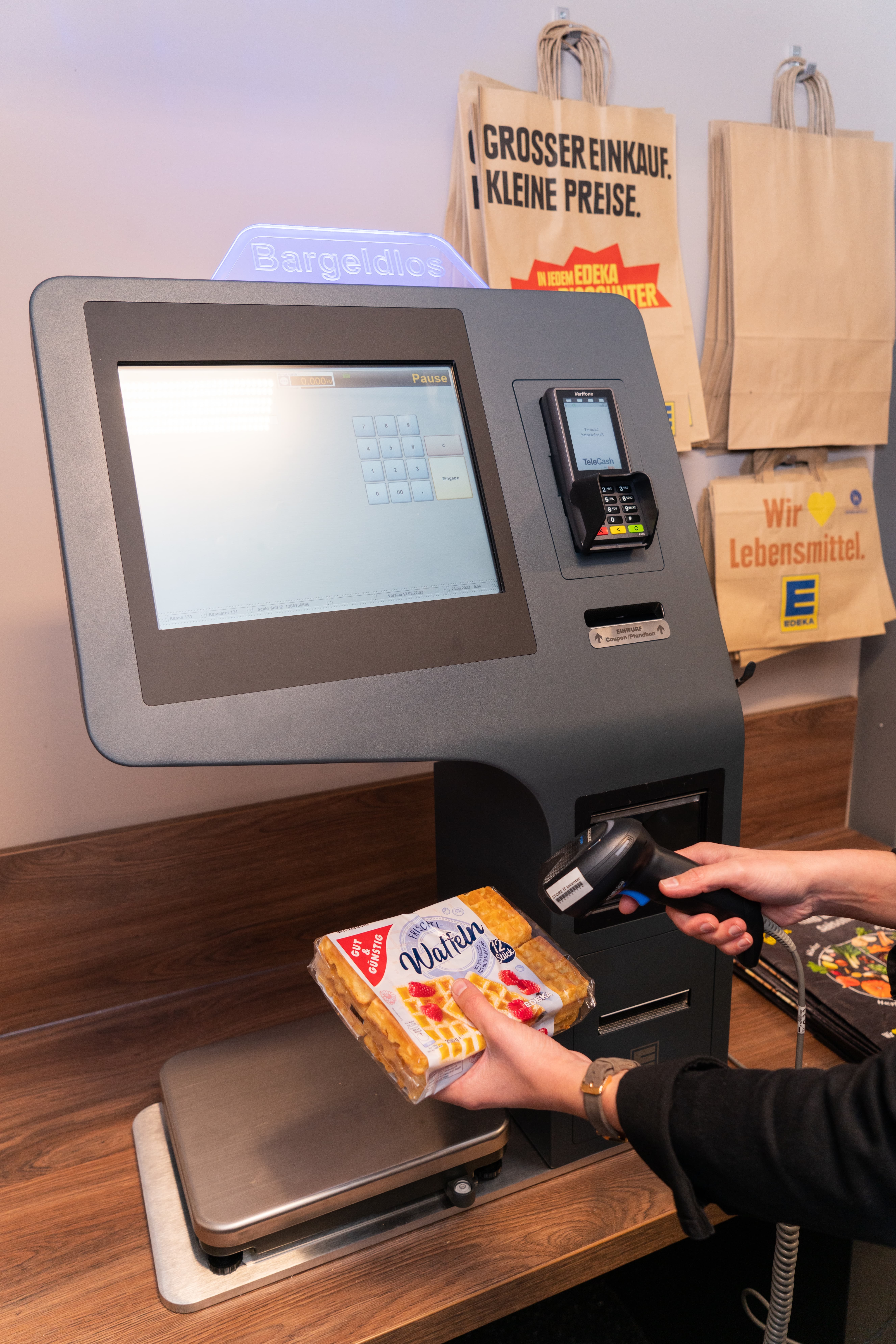 Zwei Hände die eine Packung Waffeln an einer Selbstcheck-Out-Kasse scannen.