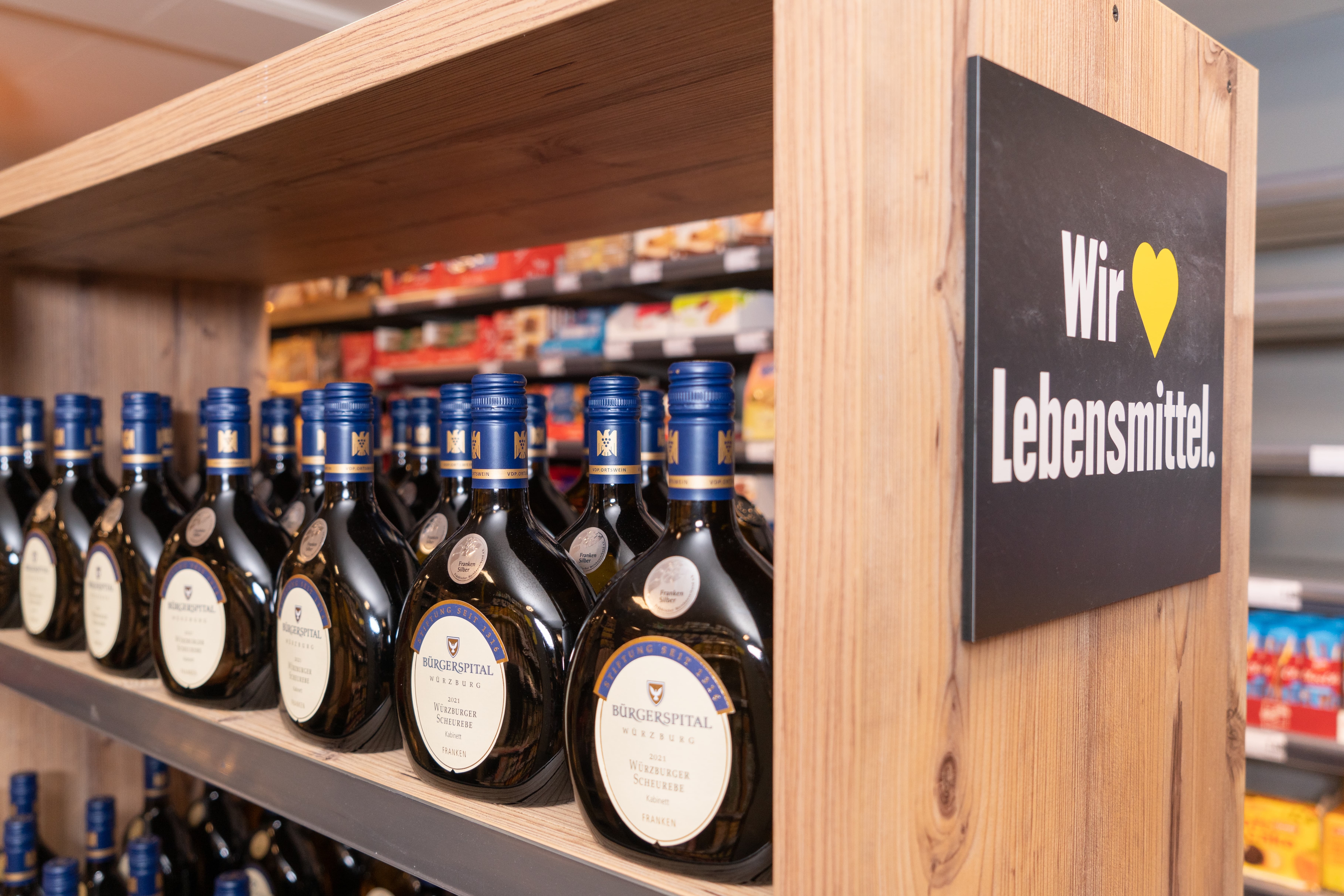 Ein Weinregal an dessen Ende ein Schild angebracht ist. Auf diesem Schild steht: "Wir lieben Lebensmittel".