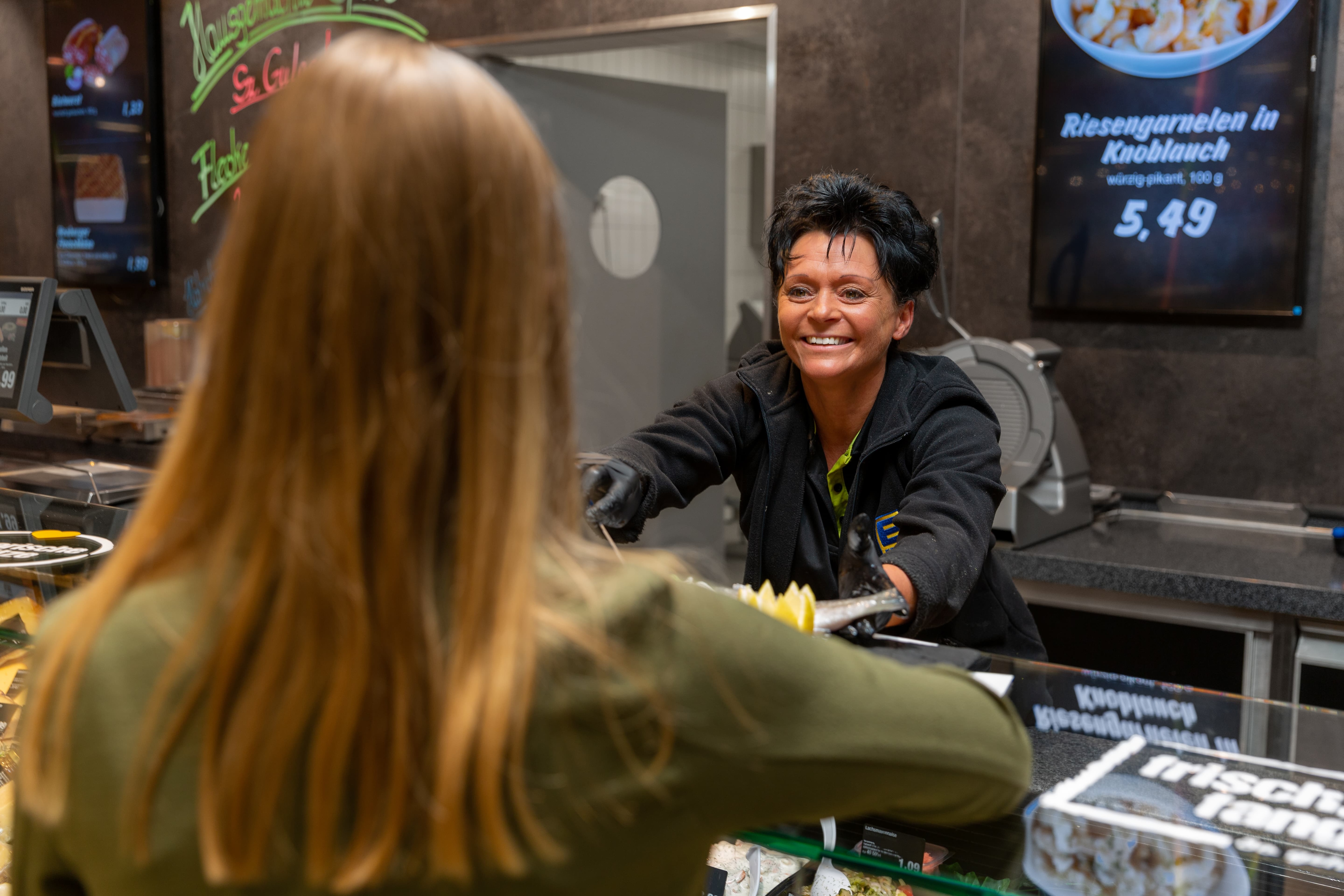 Eine lächelnde Edeka-Mitarbeiterin bedient eine Kundin an der Bedientheke.