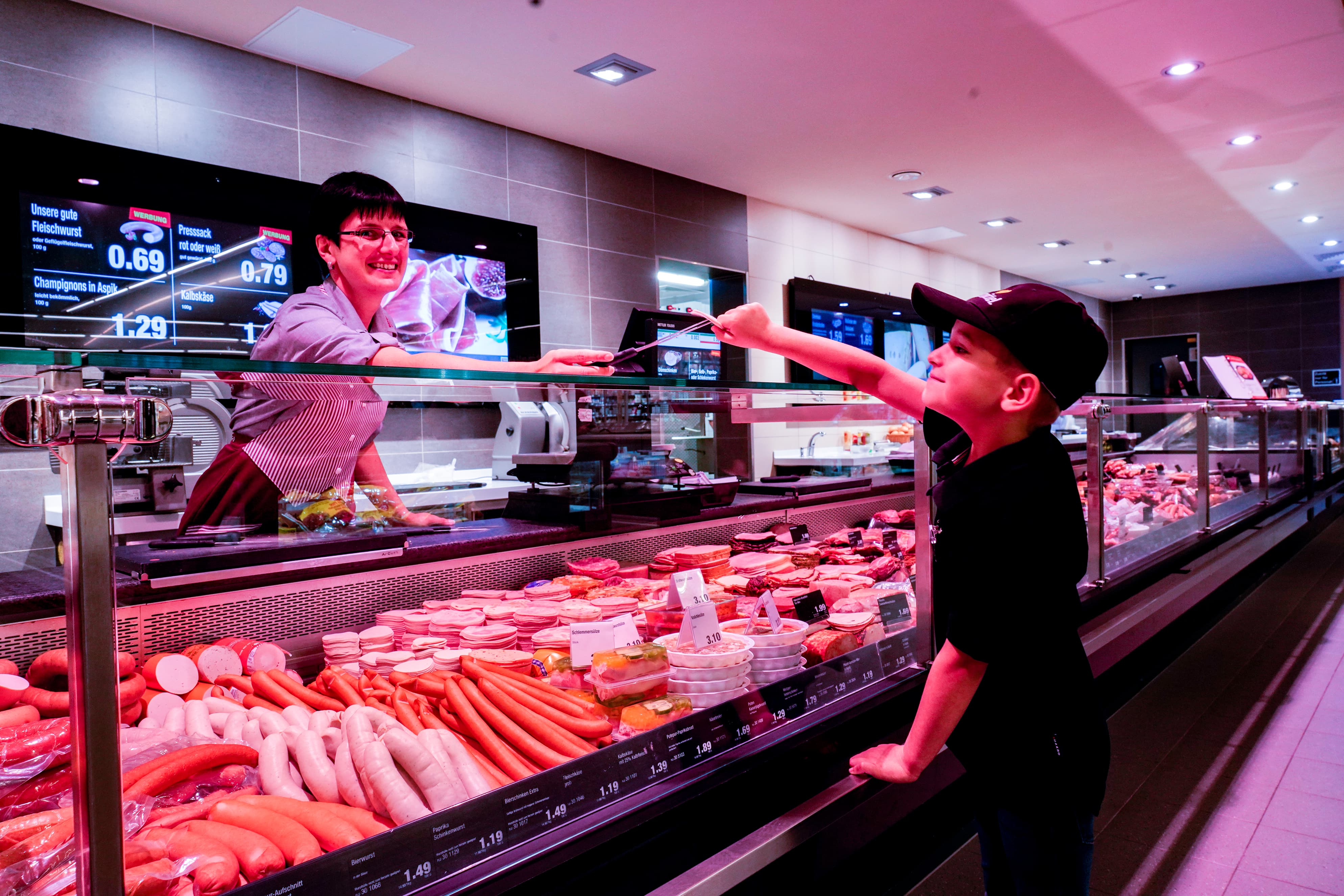 Die Bedientheke eines EDEKA-Markts. Eine Mitarbeiterin reicht einem Jungen etwas zum Probieren.