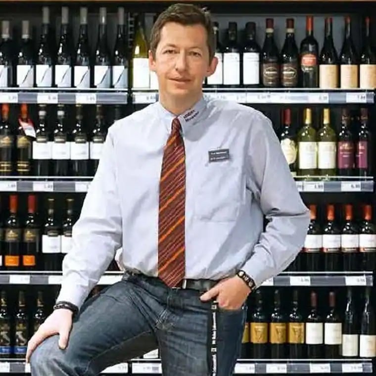 Hr. Mühlbauer steht vor dem Weinregal frontal zur Kamera gerichtet.