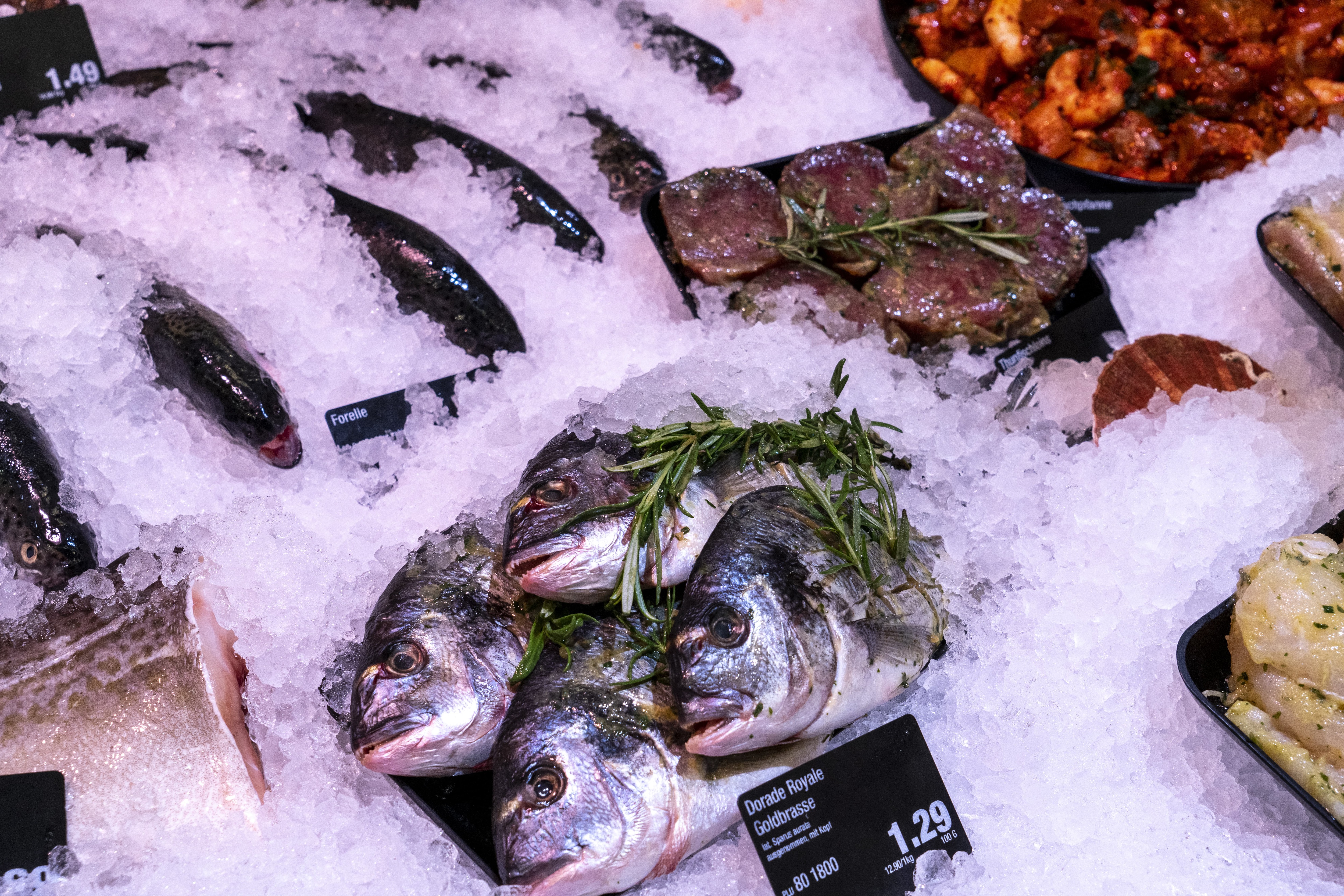 Fisch in einer Auslage im Close-Up, mit Preisschildern und Rosmarin als Deko.