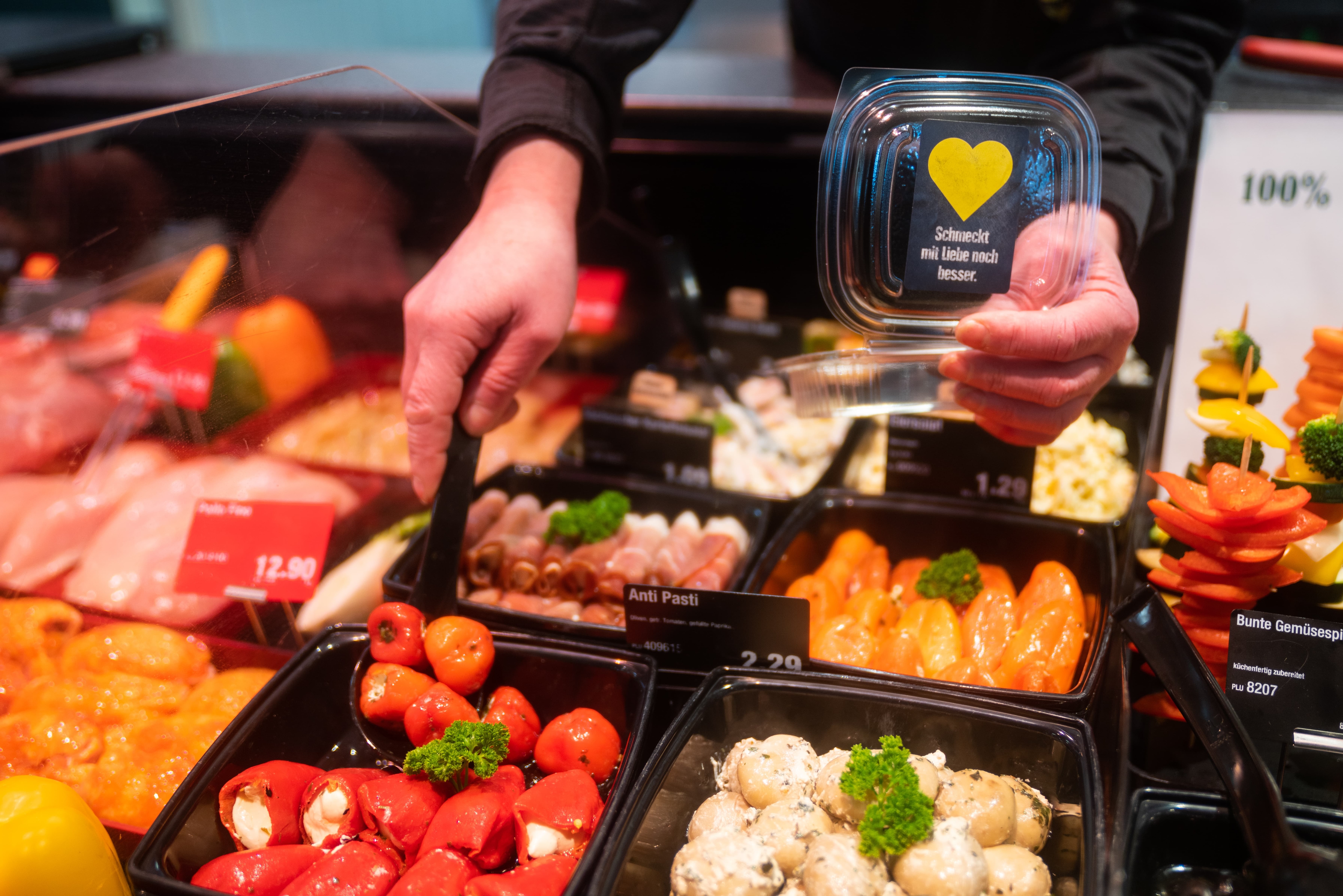 Jemand befüllt ein transparentes Plastic-Schälchen mit Antipasti von der Salatbar.