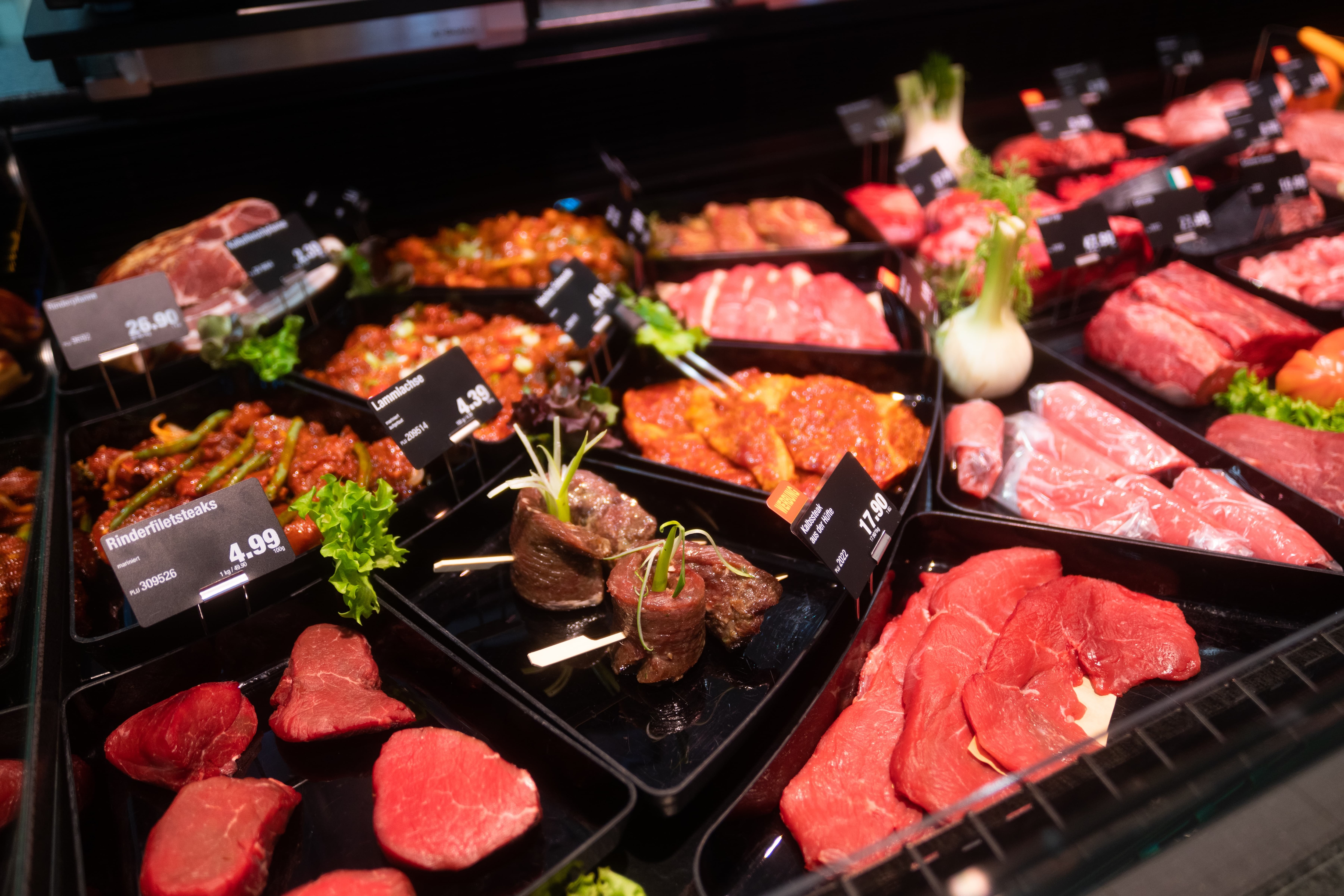 Verschiedene Fleischsorten mit Preisschildern in einer Auslage.