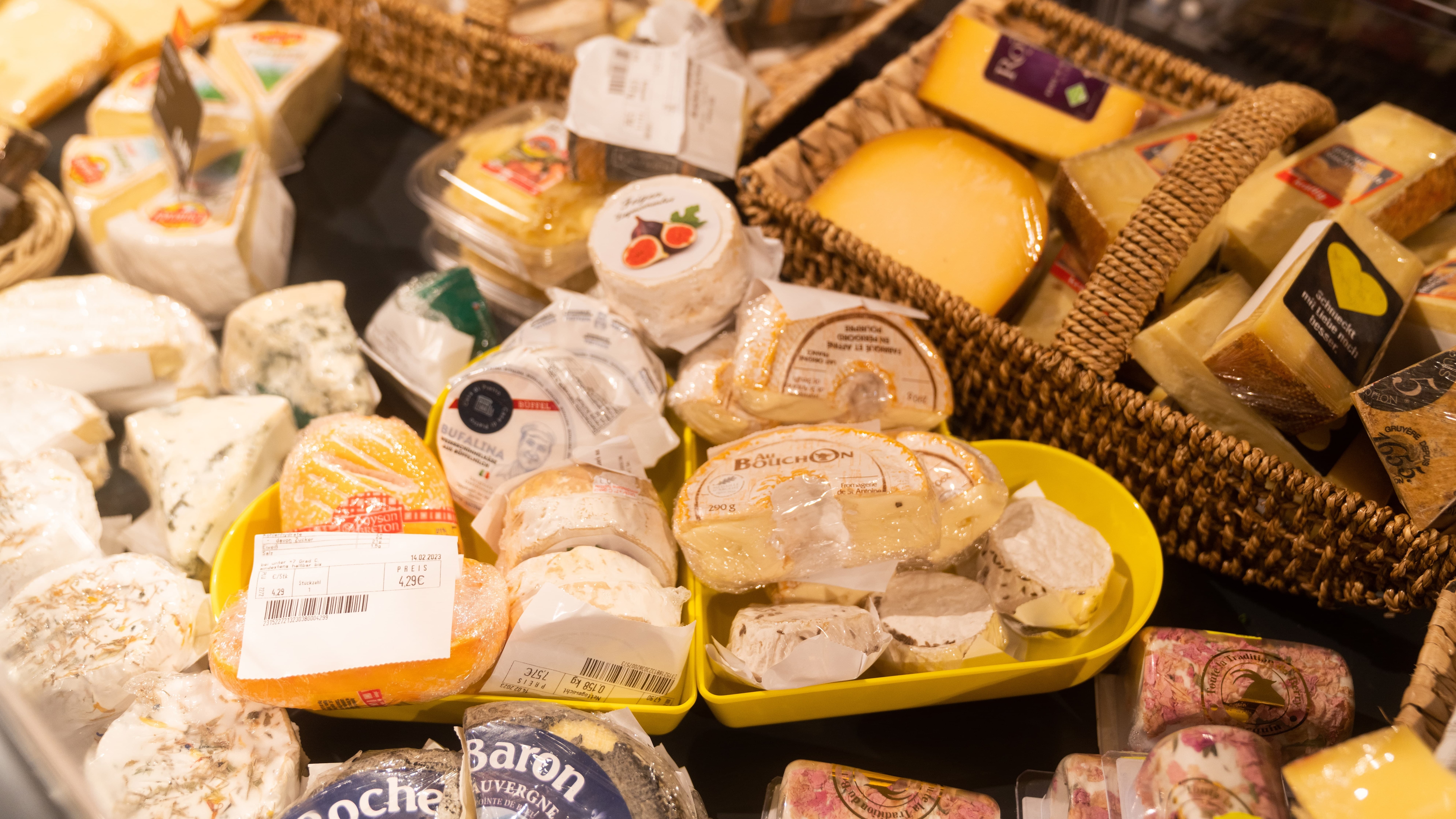 Verschiedene Käsesorten mit Preisschildern in einer Auslage.