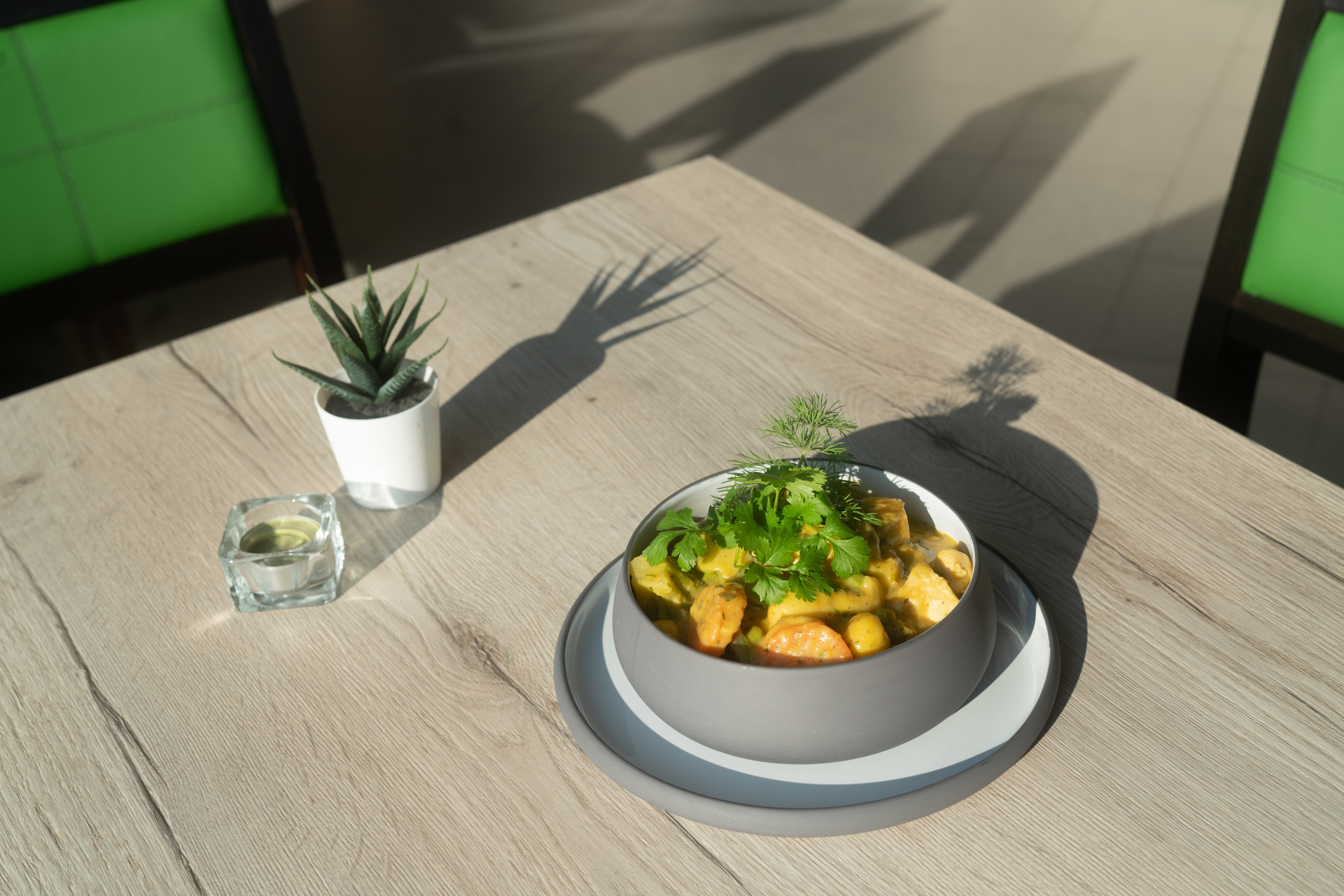 Auf einem Tisch steht ein Schälchen mit Essen. Daneben ein Teelicht und eine kleine Pflanze.