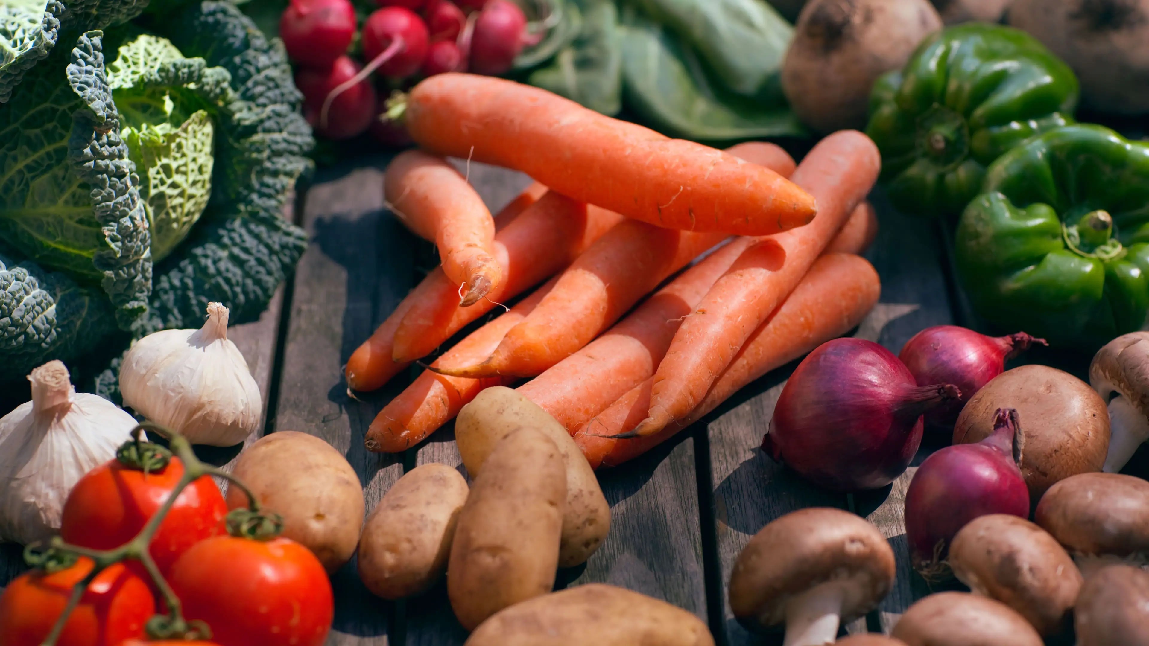 Verschiedene Gemüsesorten liegen bunt gemischt auf einem Holztisch.