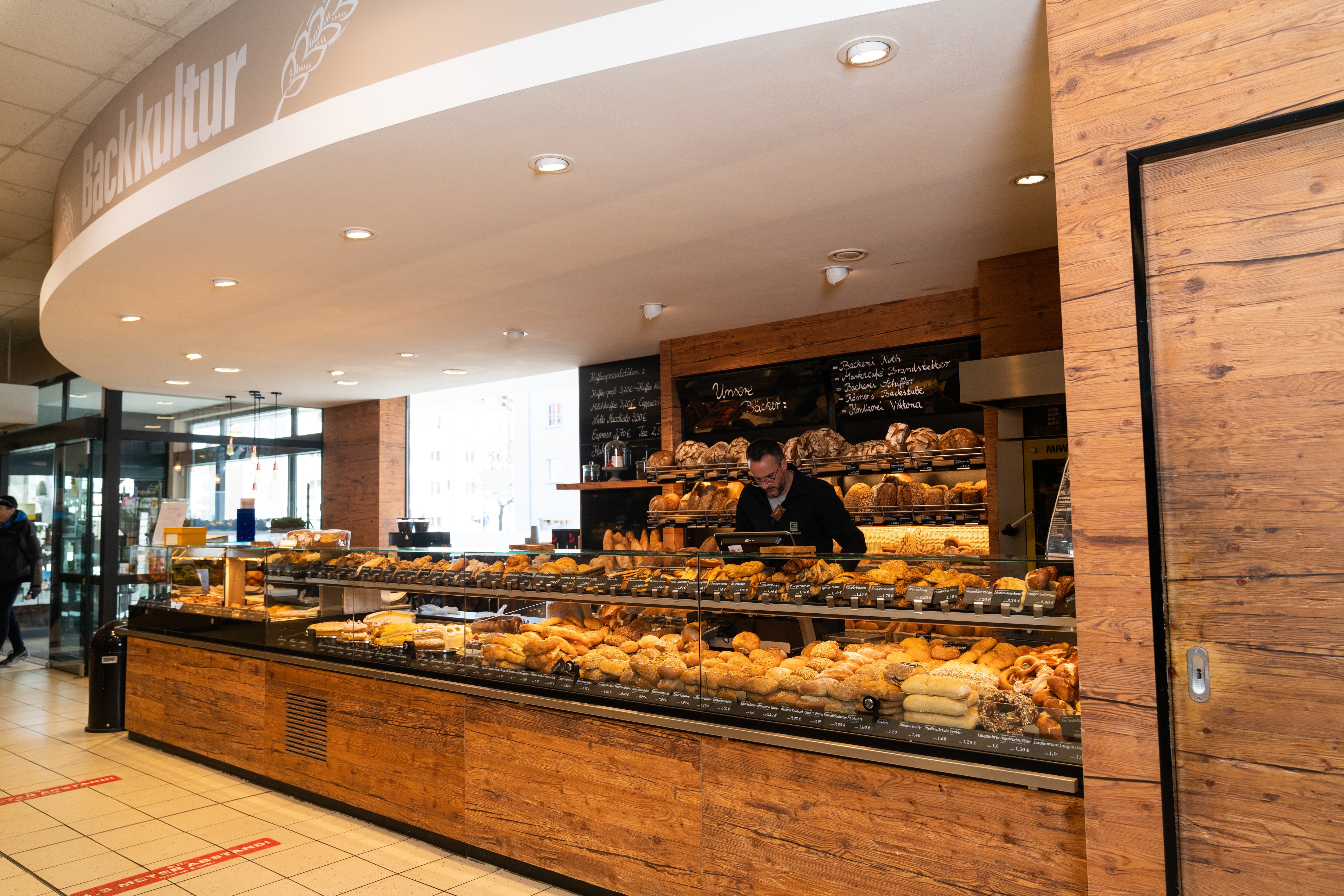 Bäckereitresen mit brauner Holzfront. Über den Deckenlichtern steht Backkultur.