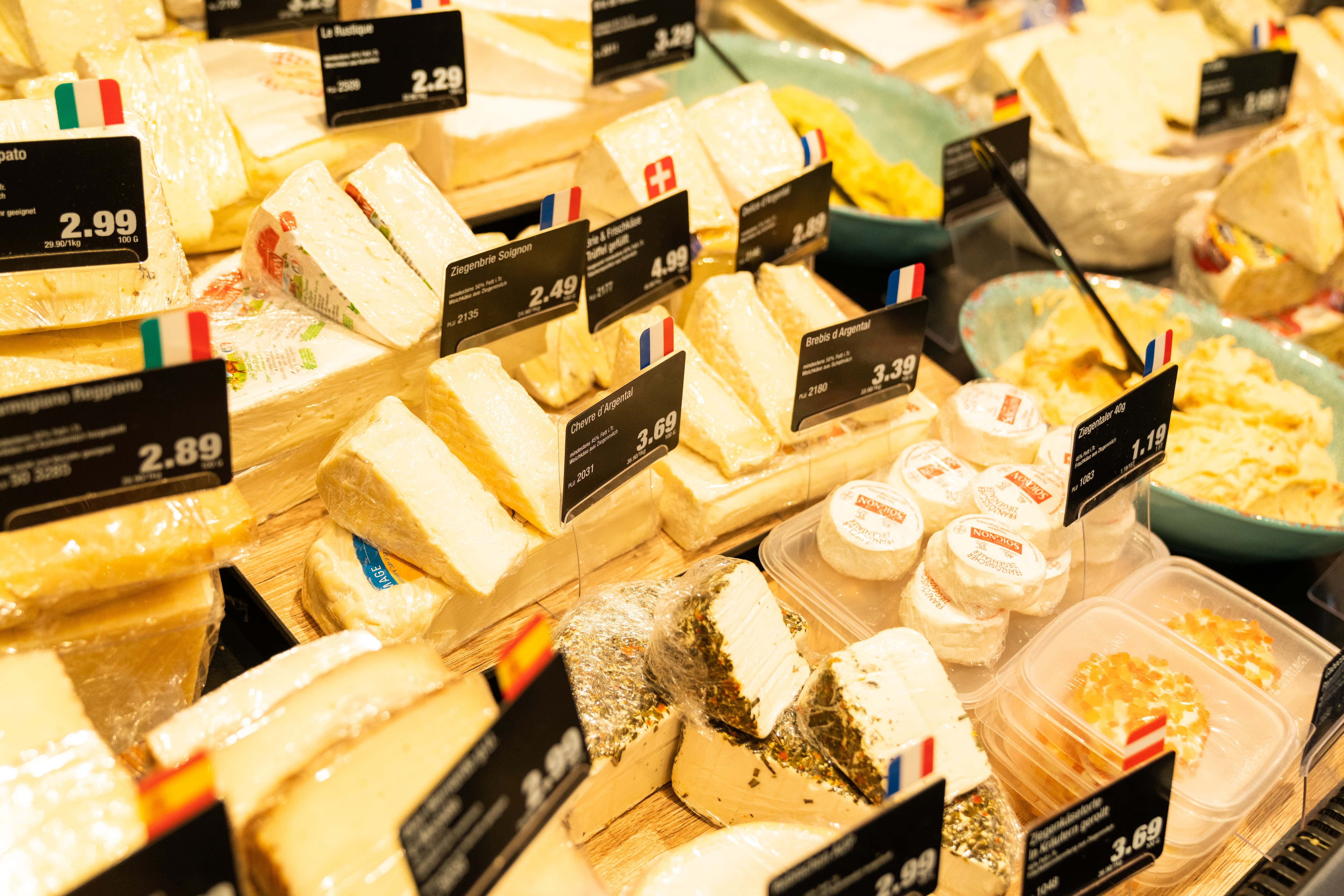 Verschiedene Käsesorten mit Preisschildern in einer Auslage.