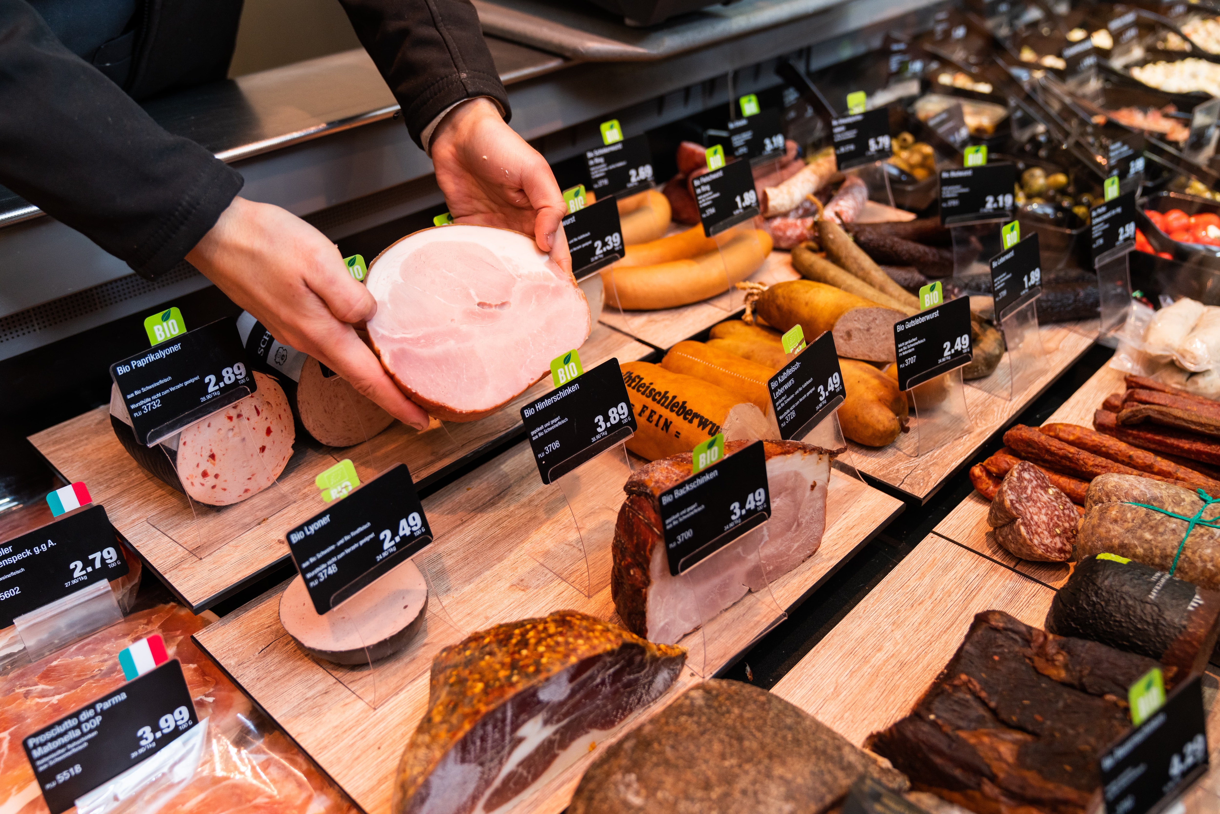 Zwei Hände halten einen gekochten Schinken hoch über der Frischetheke.