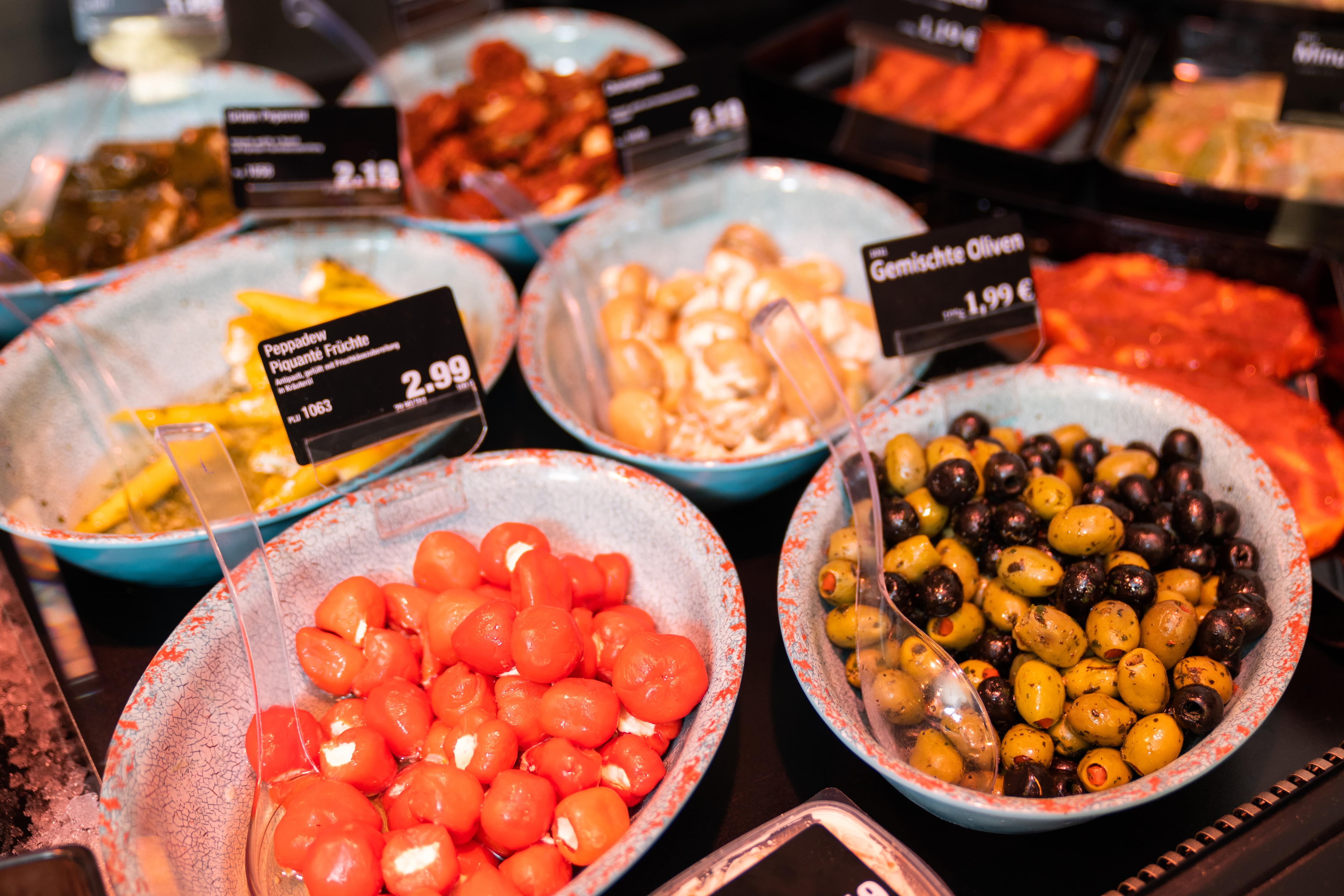 Schälchen mit ANtipasti und Preisschildern, unter anderem Peppadew und gemischte Oliven.