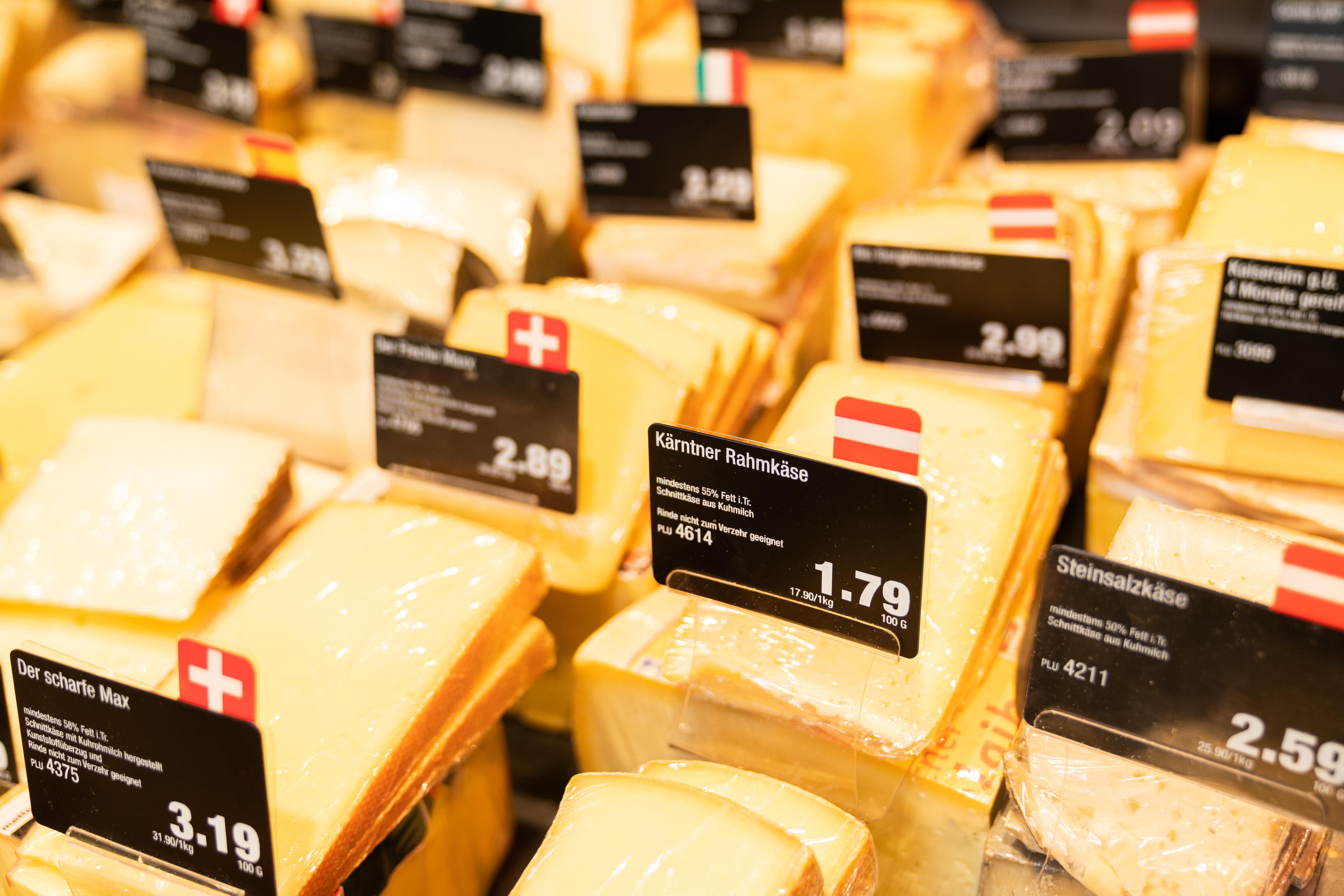 Verschiedene Käsesorten mit Preisschildern in einer Auslage.