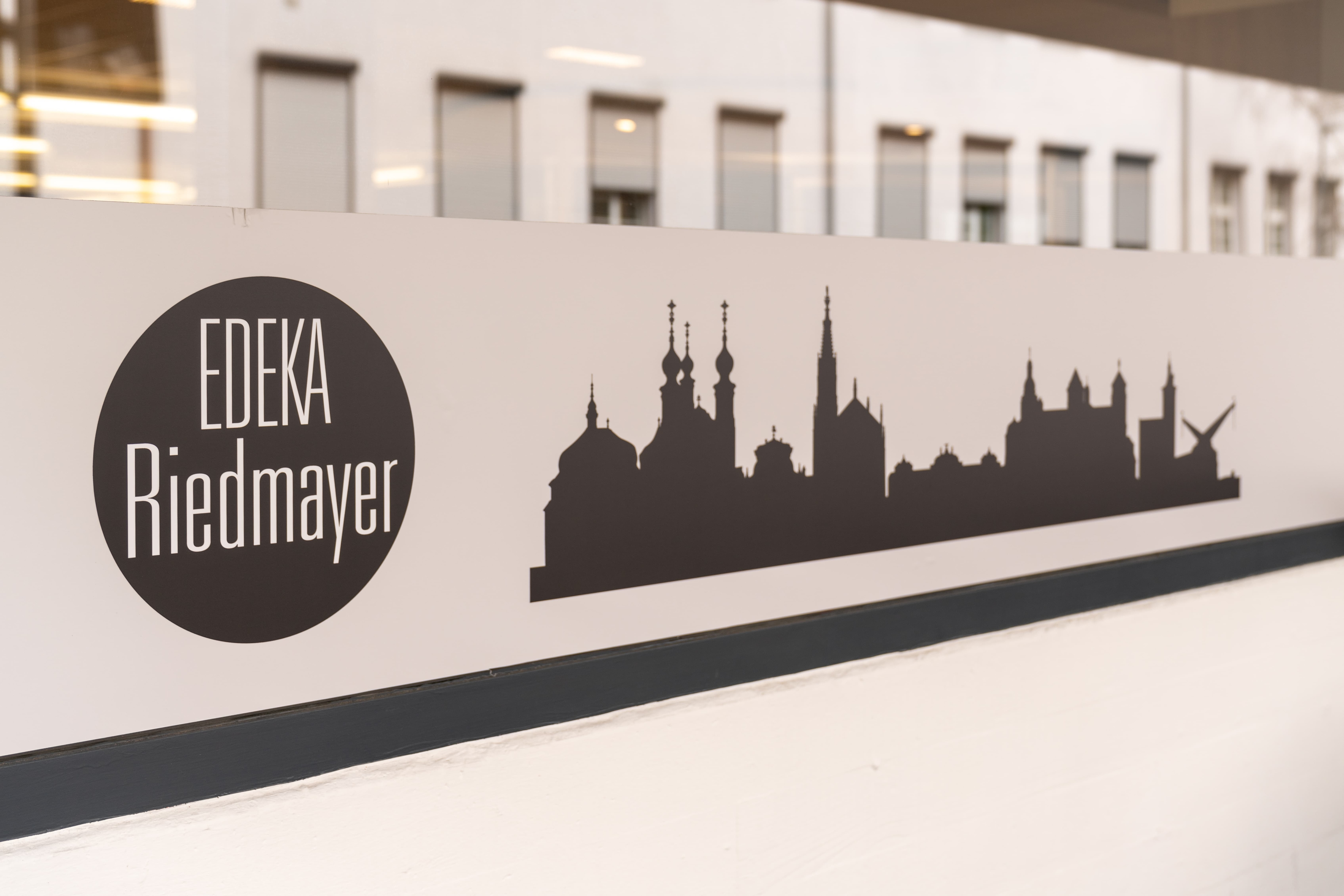 An einer Scheibe ist ein Aufkleber mit EDEKA Riedmayer-Logo und der Silhouette einer Stadt.