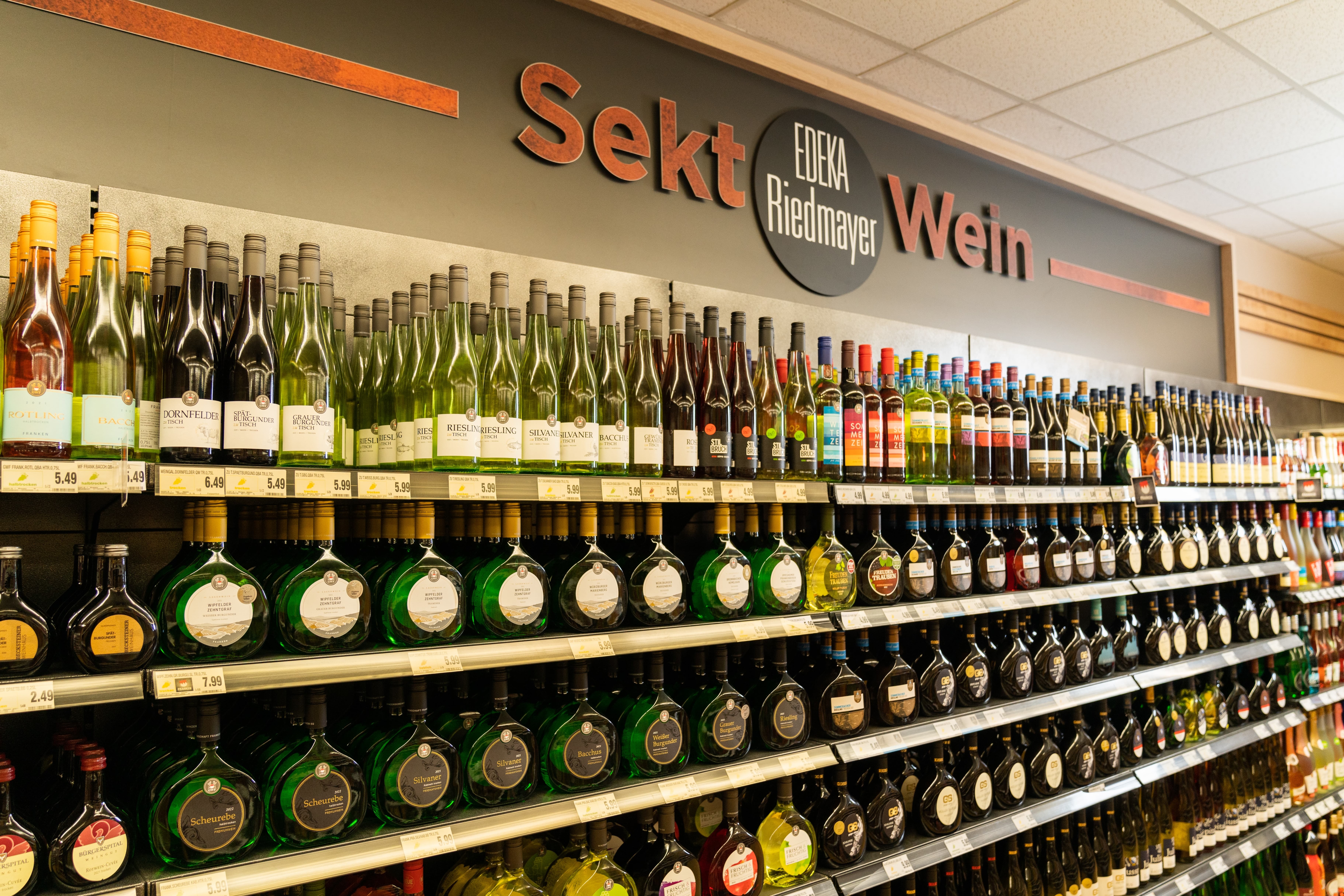 Über dem Weinregal steht Sekt, EDEKA Riedmayer Wein.