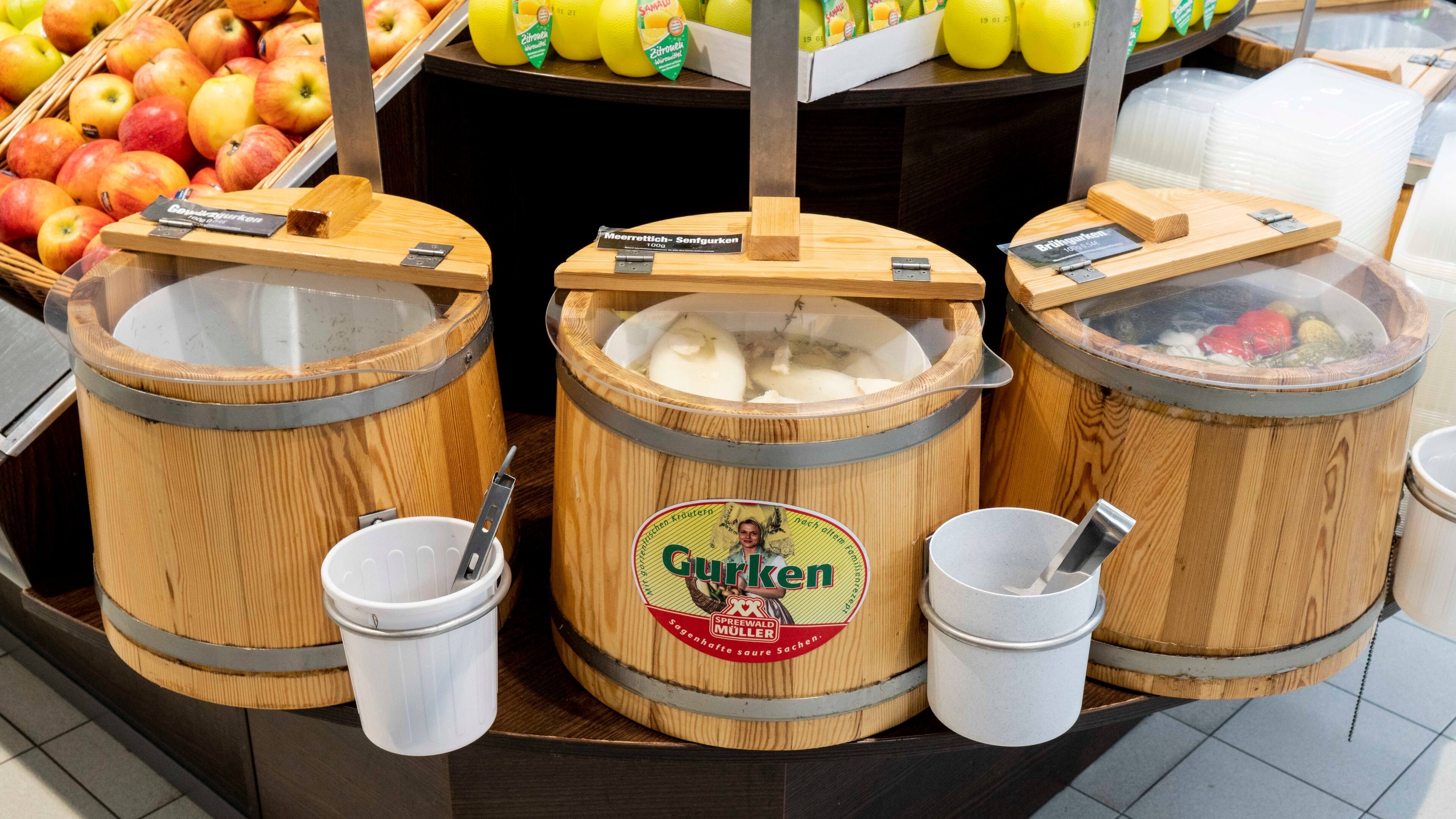 Drei kleine Fässer mit verschiedenen eingelegten Gurken in einer Obst- und Gemüseabteilung.
