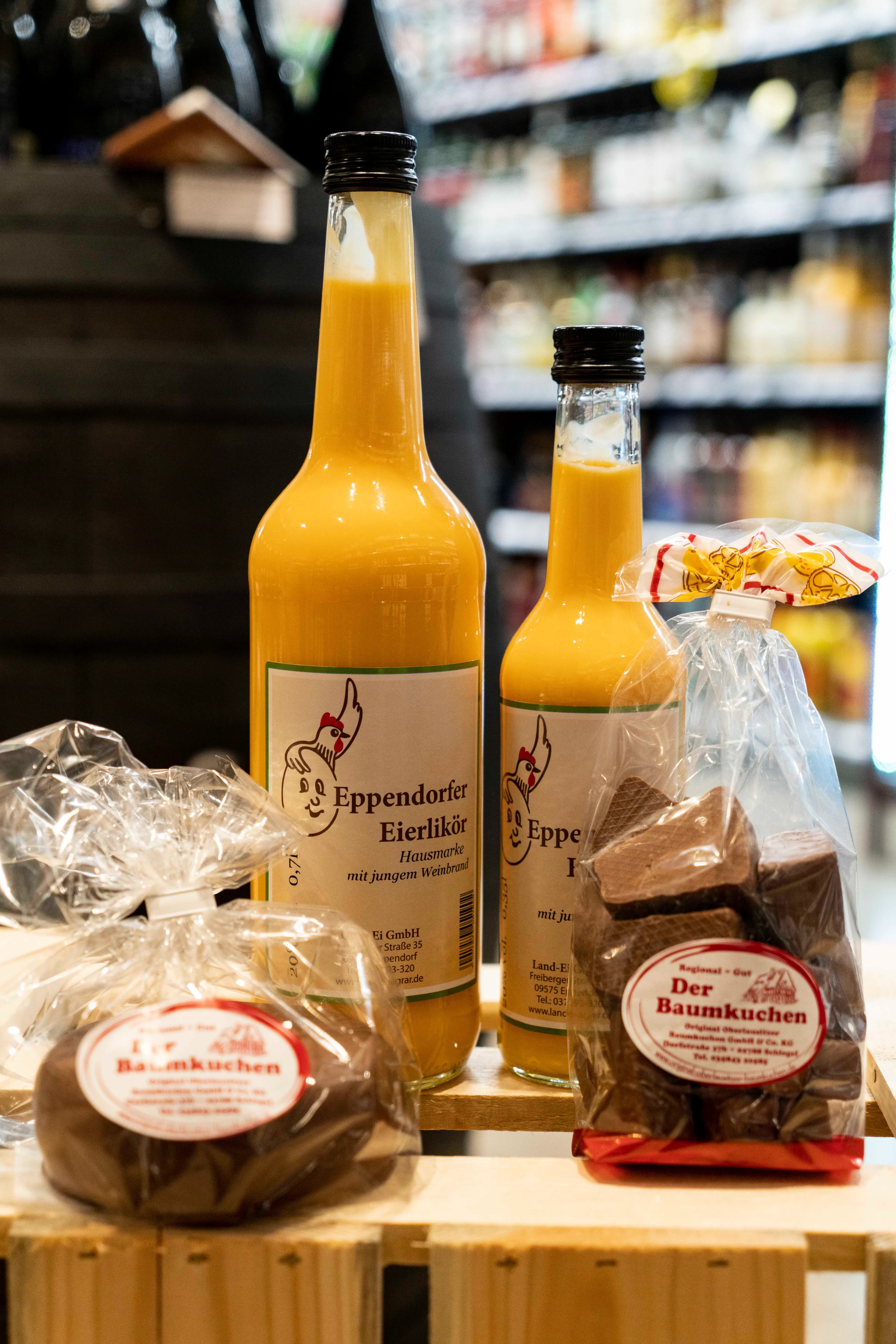 Zwei Flaschen mit regionalem Eierlikör und zwei Tüten Baumkuchen auf einer Holzkiste.