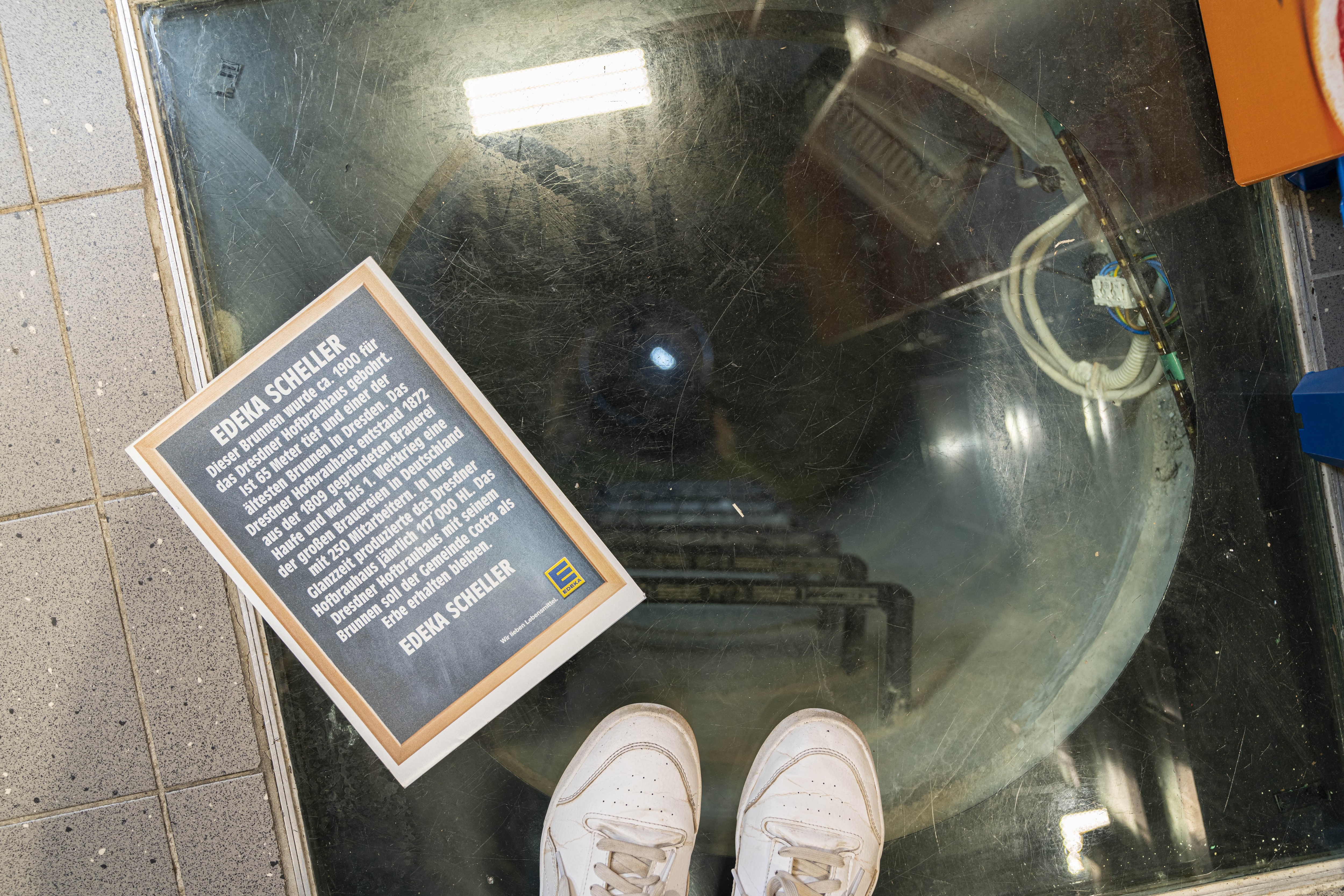 Durch eine gläserne Bodenplatte sieht man eine Treppe, die tief in den Boden führt.